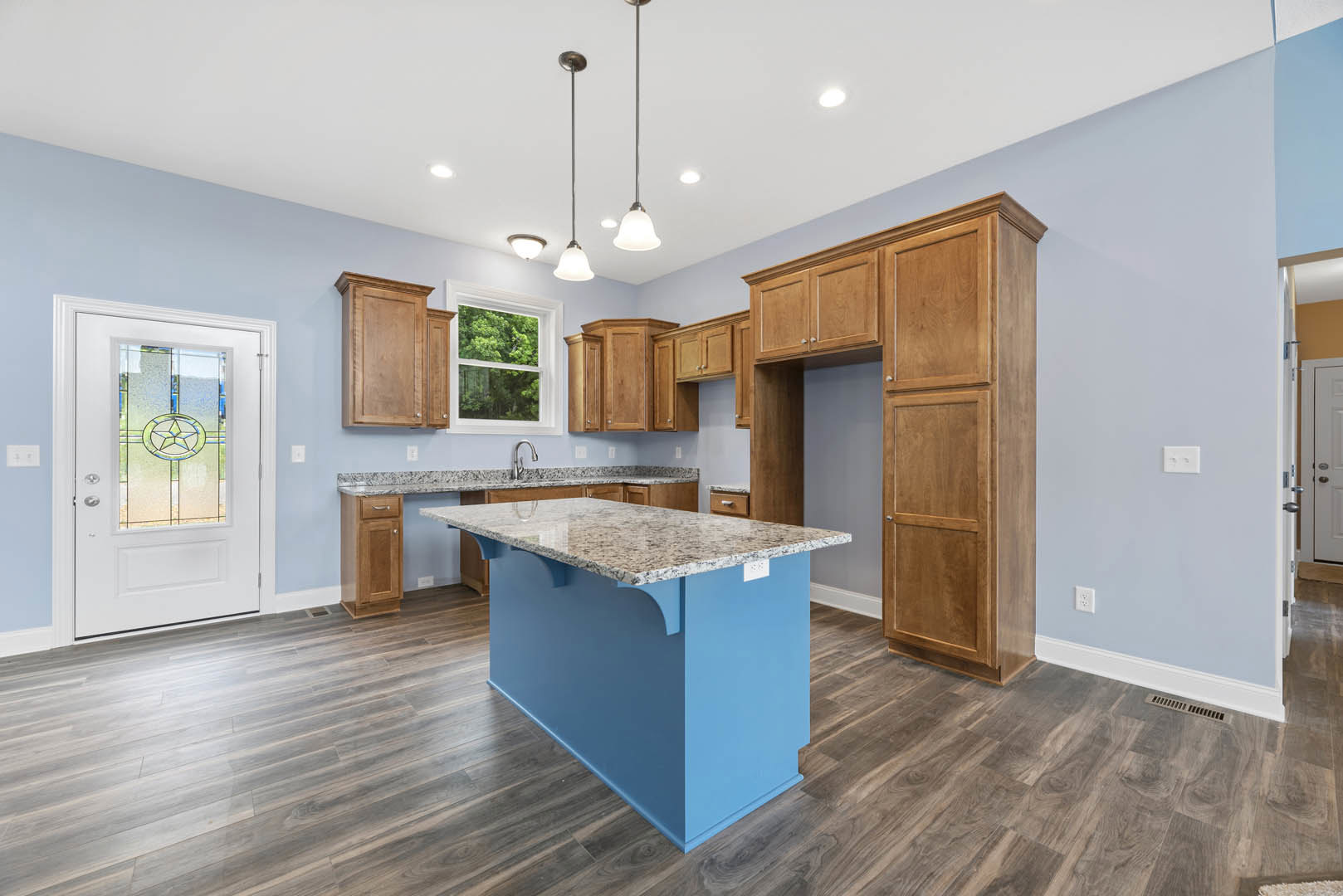Blue kitchen island with marble countertop, wood cabinets, white door featuring star design, window overlooking trees, light hardwood flooring