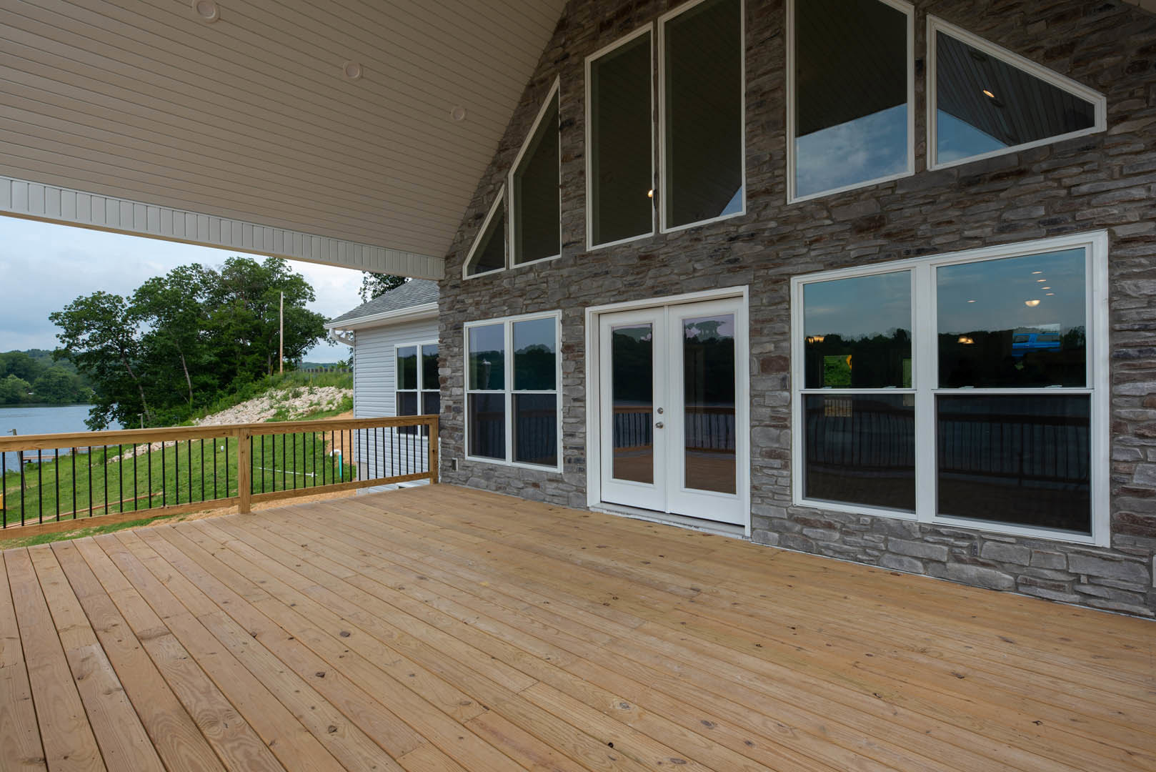 Spacious two-story home with wooden deck featuring black railing, glass doors, and white double entry flanked by mirrored panel; screened window on side, surrounded by trees on