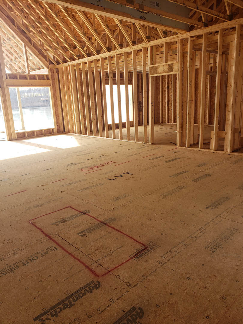Exposed wood framing with beams and planks, subfloor marked with red lines, construction materials and insulation visible in unfinished interior