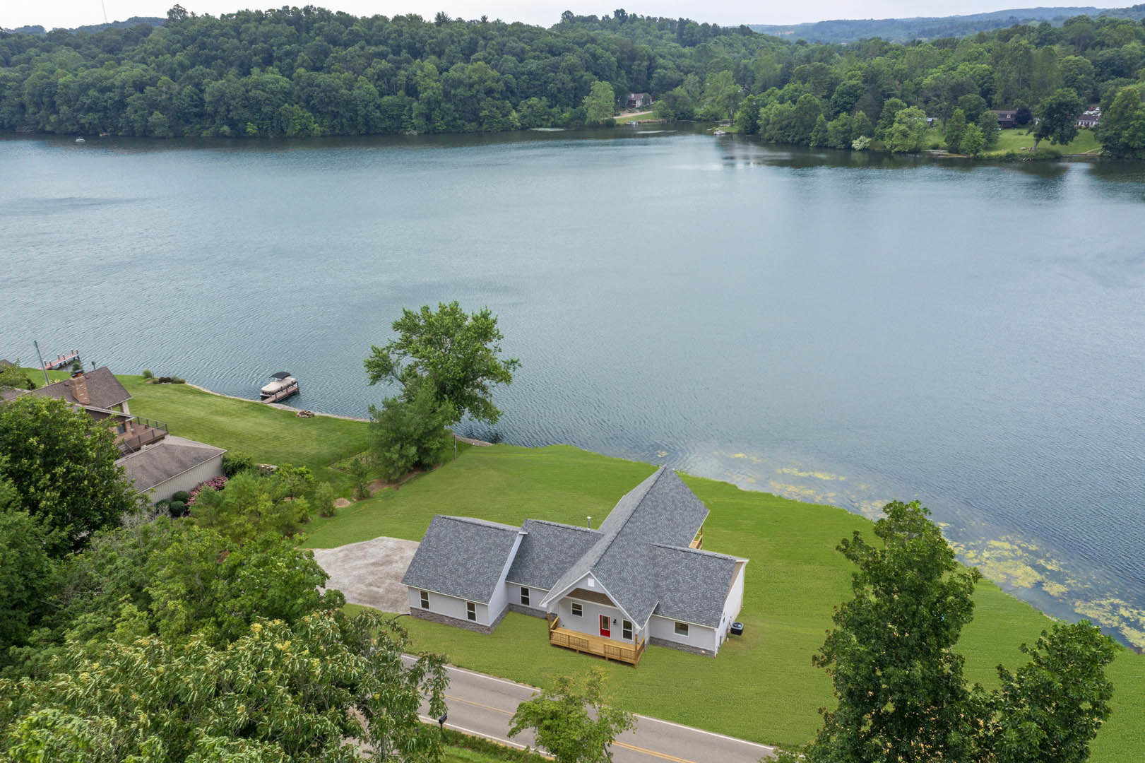 Modern lakeside home with large windows, manicured lawn, mature tree, and a boat docked on calm water