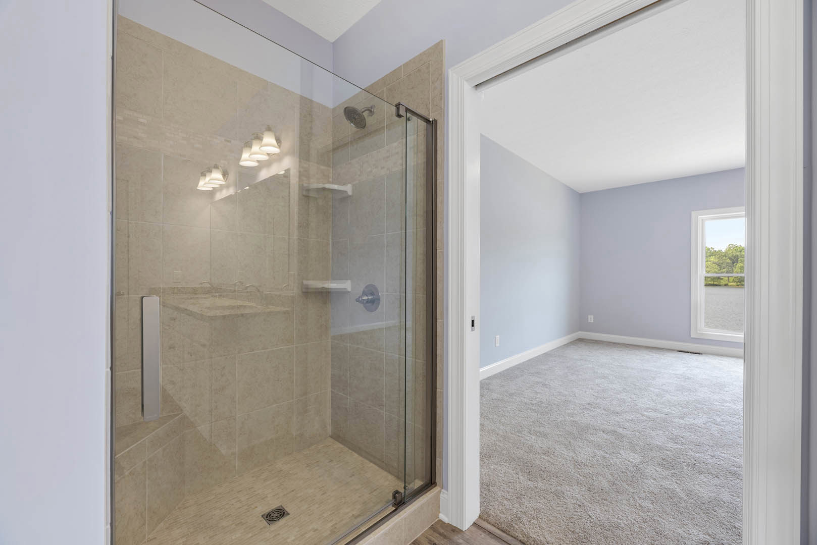 Glass shower enclosure with chrome fixtures, marble tile walls, and a window overlooking trees in a modern bathroom