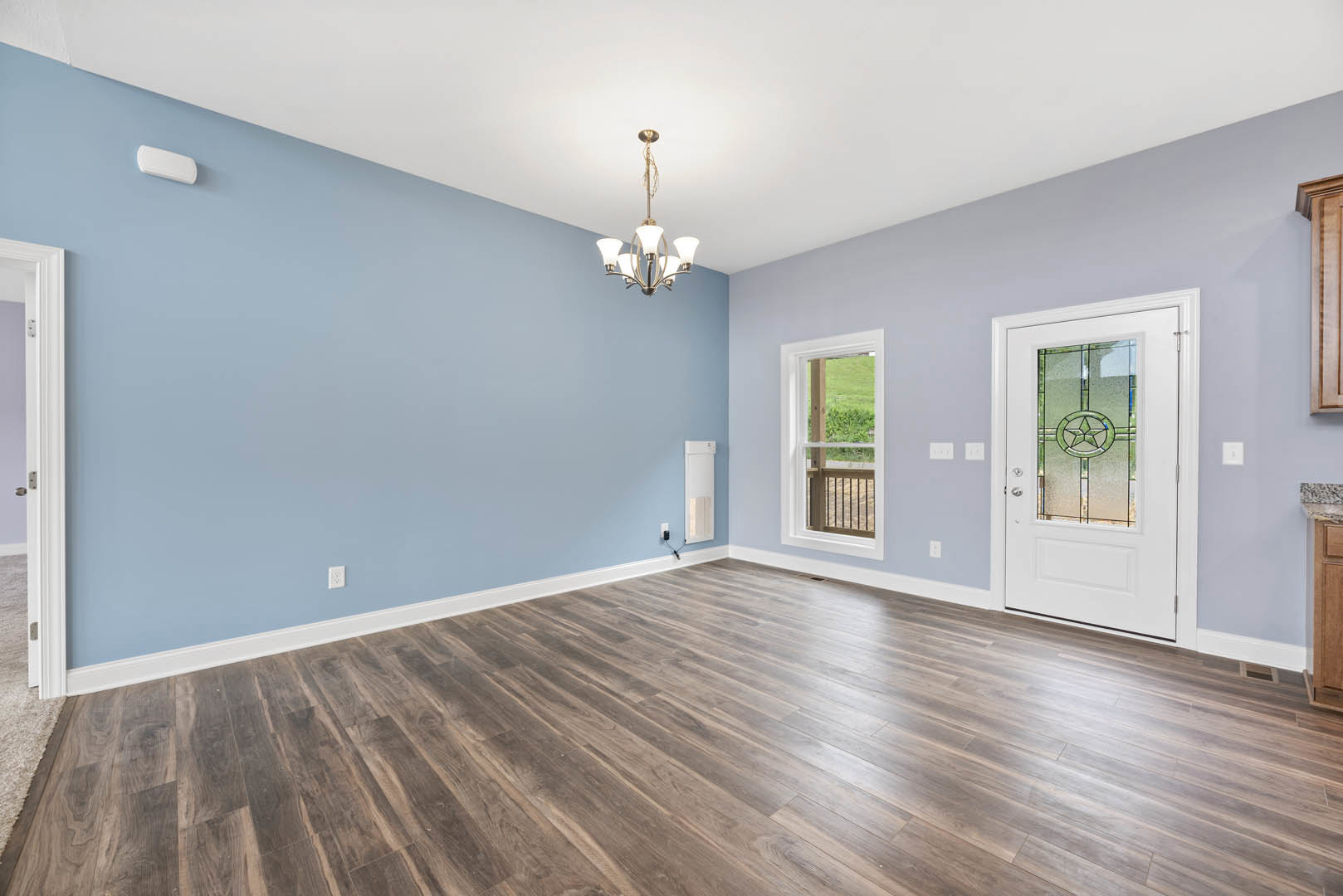 Room with hardwood floor, white door featuring a star detail, chandelier overhead, large glass window overlooking grassy yard and fence