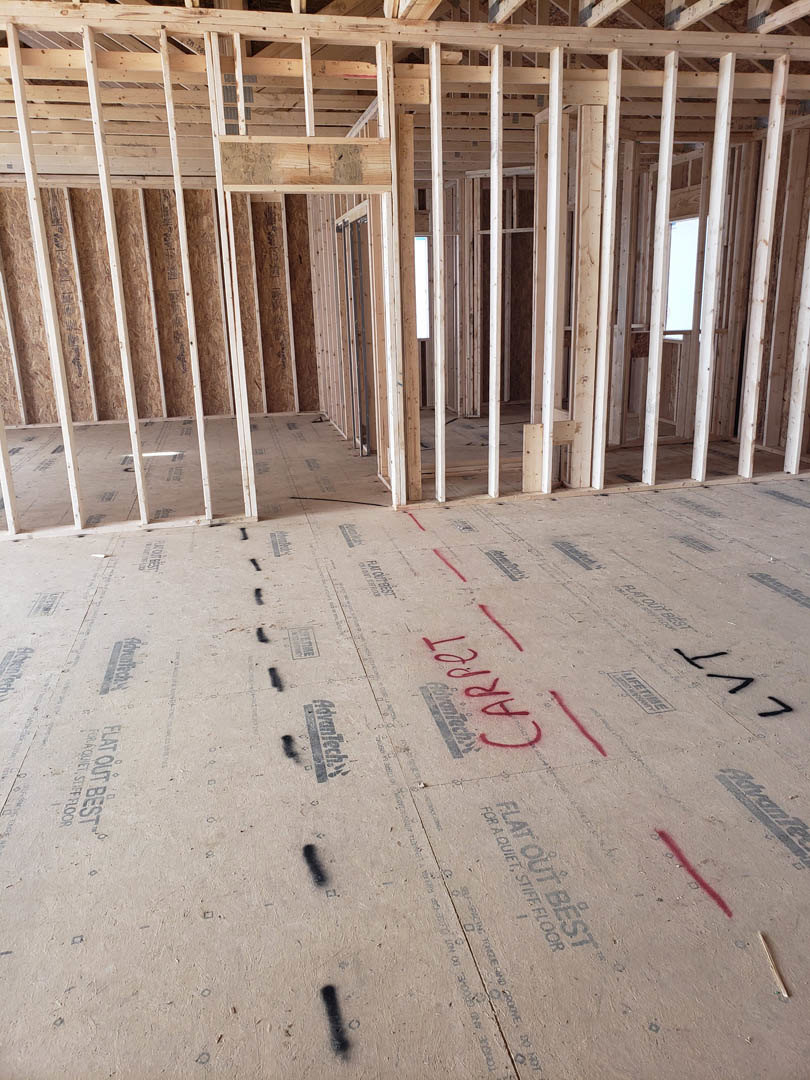 Unfinished room with exposed wood framing, construction insulation, and red writing marked on subfloor