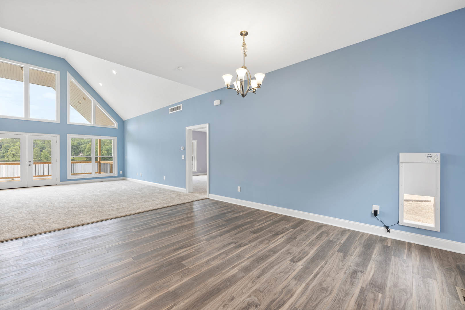 Spacious room with hardwood flooring, white paneled door, blue accent wall, plaster ceiling, and modern chandelier
