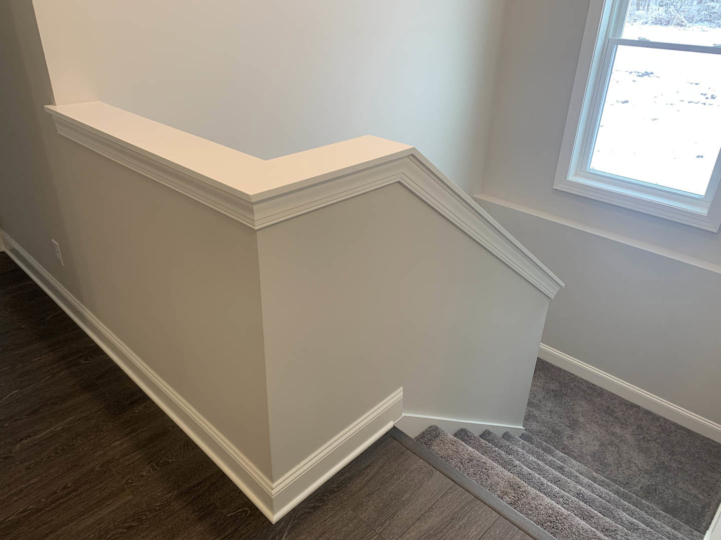 Carpeted staircase with white walls, wood flooring, and a window with a white frame in a residential interior
