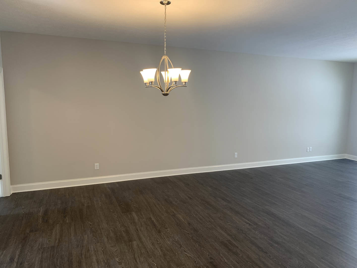 Chandelier with crystal accents hanging from white plaster ceiling above dark hardwood floor in spacious room with neutral walls