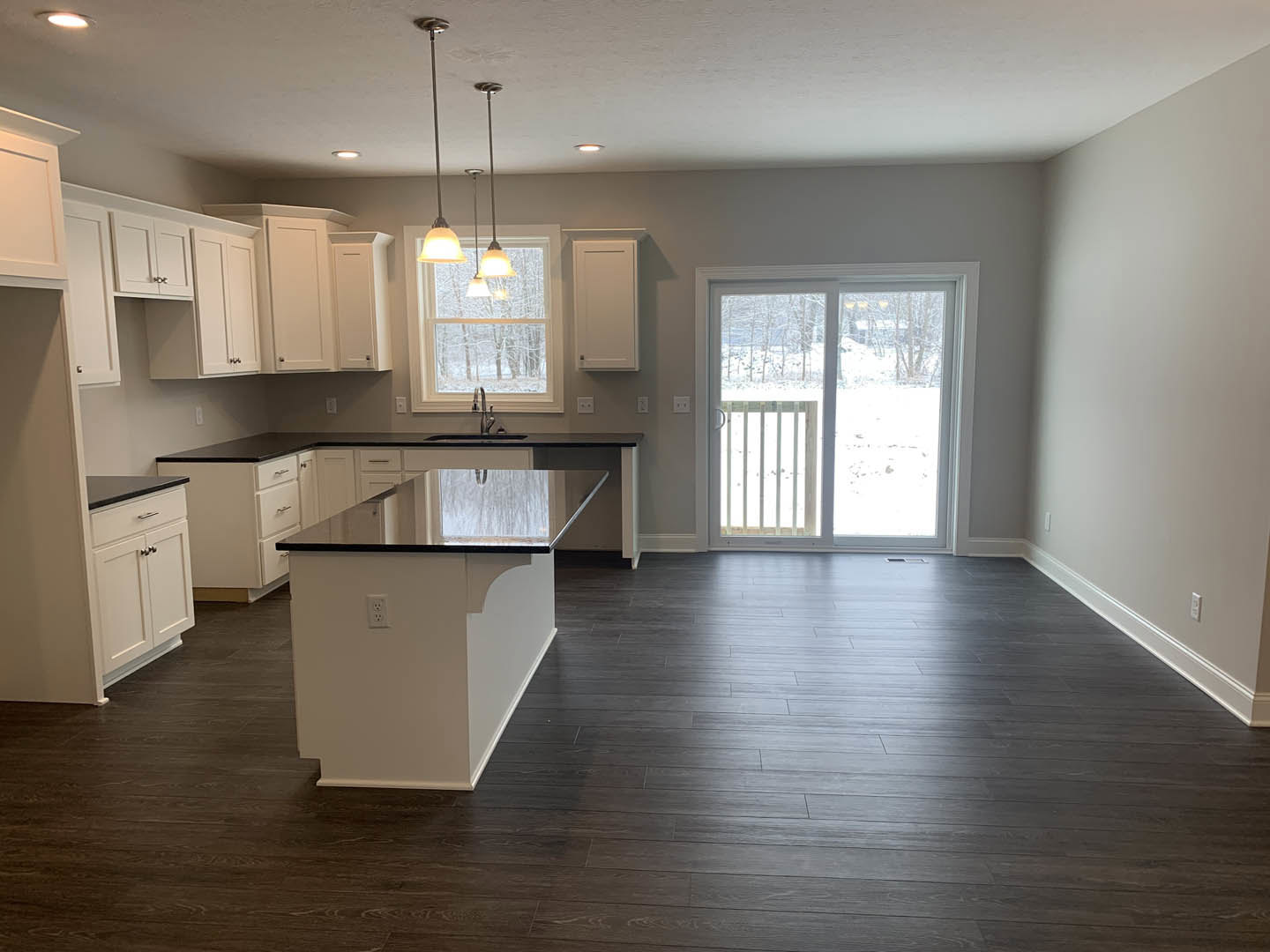 Kitchen featuring black countertops, white cabinetry with silver knobs, white island with black countertop, dark hardwood flooring, sliding glass door and window overlooking snowy