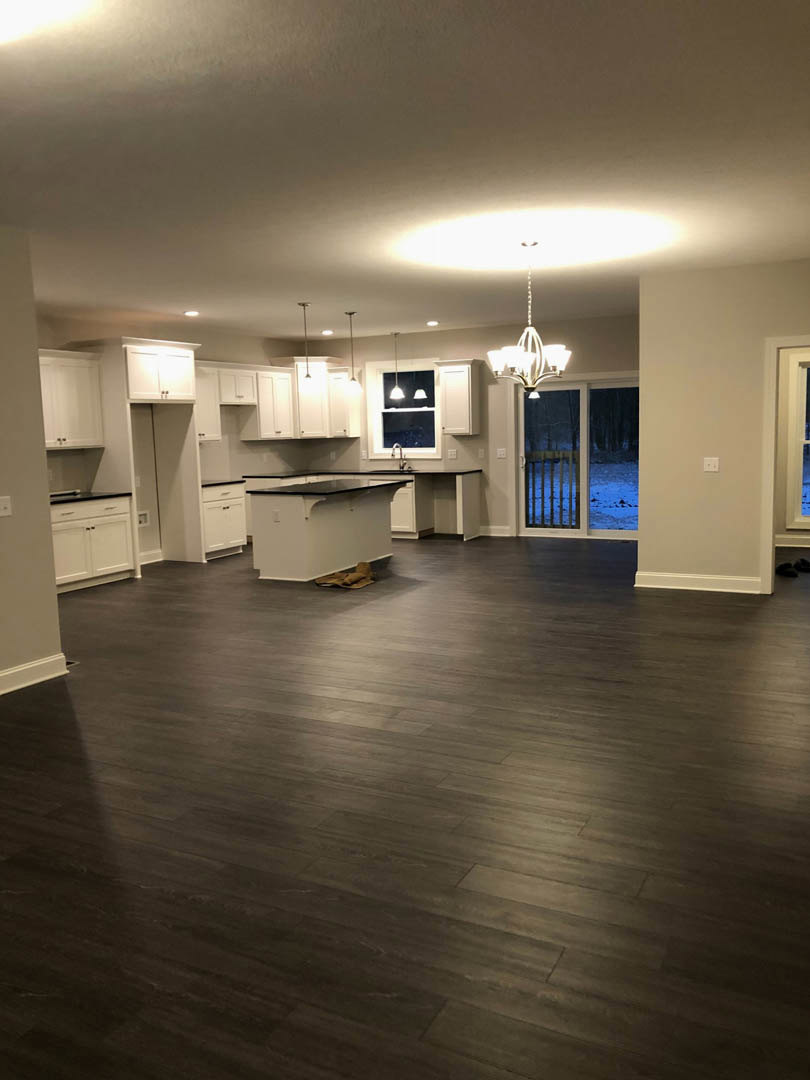 Large kitchen featuring dark hardwood floors, white cabinetry with black countertops, white walls, glass door, ceiling chandelier, and recessed lighting.