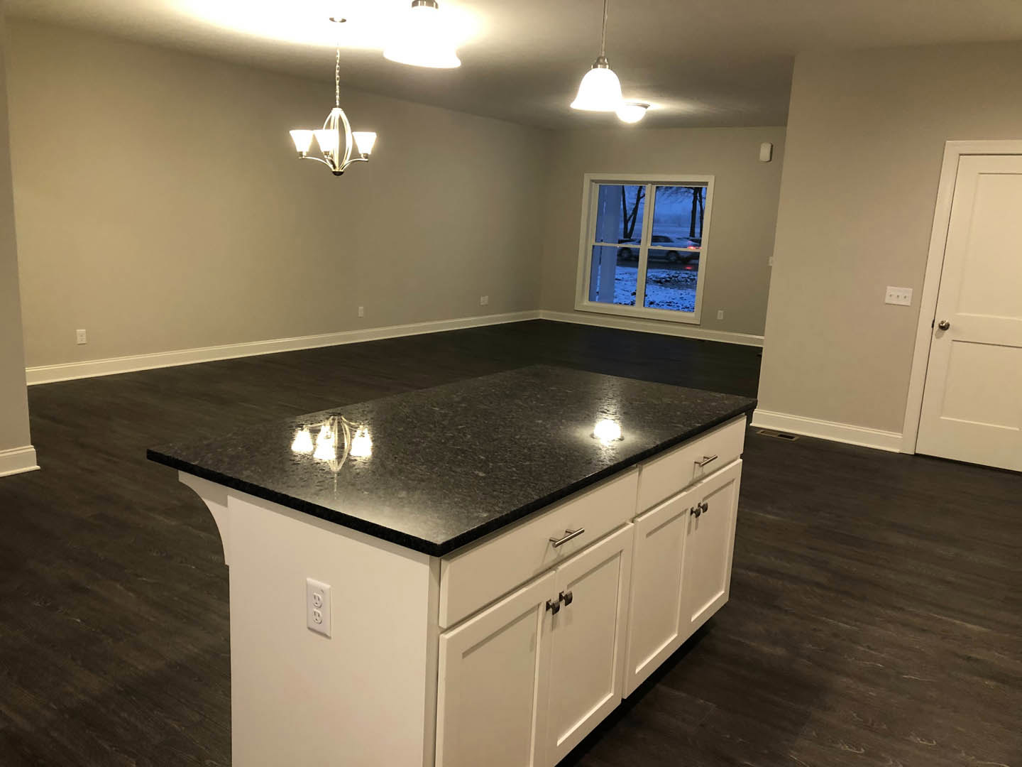 Quartz kitchen island with pendant lights, white cabinetry, stainless steel sink, tile backsplash, and window overlooking snowy street with parked cars