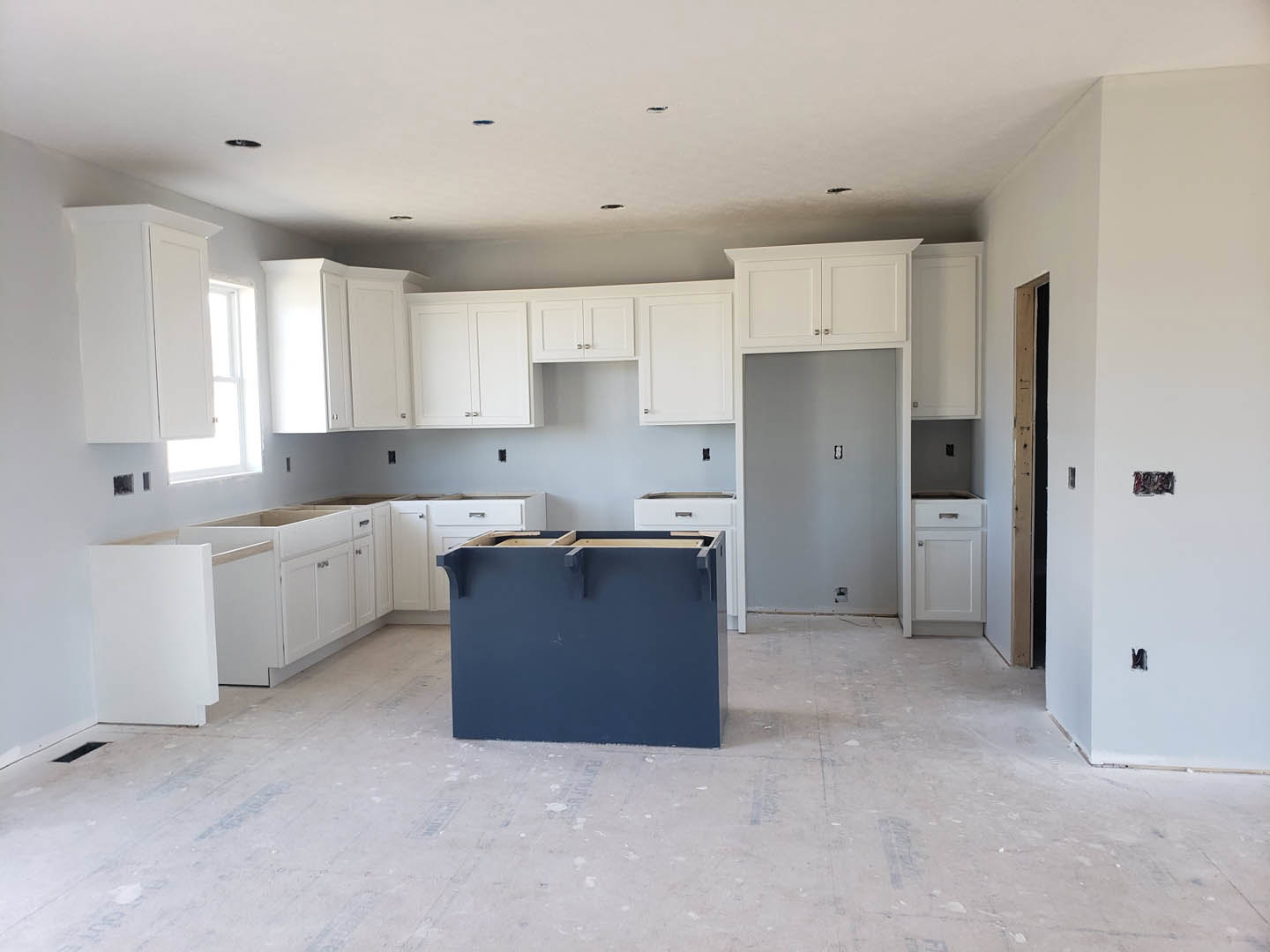 Kitchen featuring white shaker cabinets, a blue island with quartz countertop, stainless steel sink, light hardwood flooring, and recessed lighting