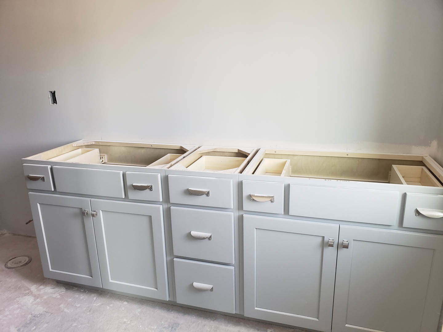 White kitchen cabinetry with silver handles, drawers, and cupboard doors, set against a light-colored wall and floor.
