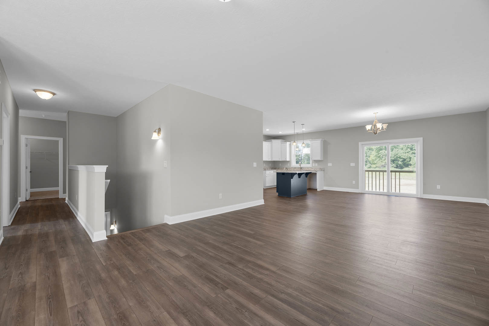 Spacious room with light hardwood floors, open kitchen area, white walls, ceiling light fixture, sliding glass door with railing, and white interior door