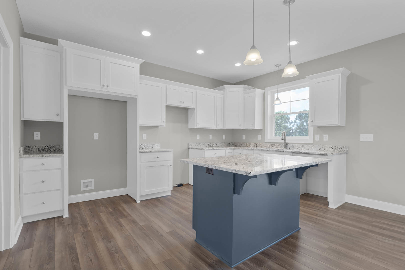 Marble-topped kitchen island with built-in sink, white cabinetry with silver hardware, pendant light fixture overhead, tiled floor, and neutral walls.