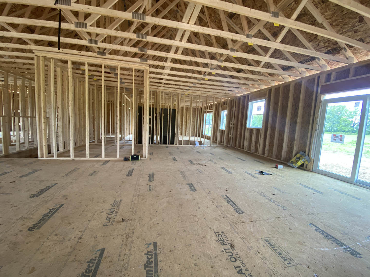Room with exposed wood ceiling beams, large windows, unfinished subfloor, and construction materials visible; skateboard resting on floor.