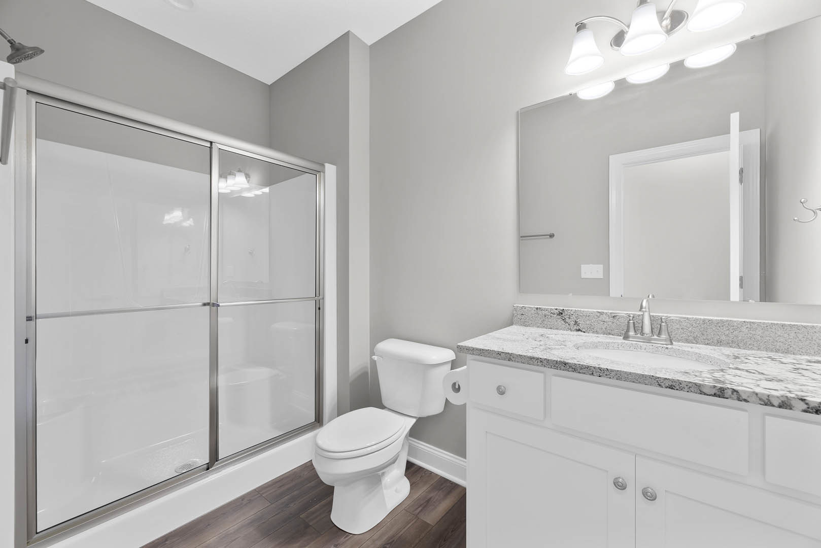 Modern bathroom with glass-enclosed shower, white toilet with lid up, light fixture above, neutral tile walls, and sleek plumbing fixtures