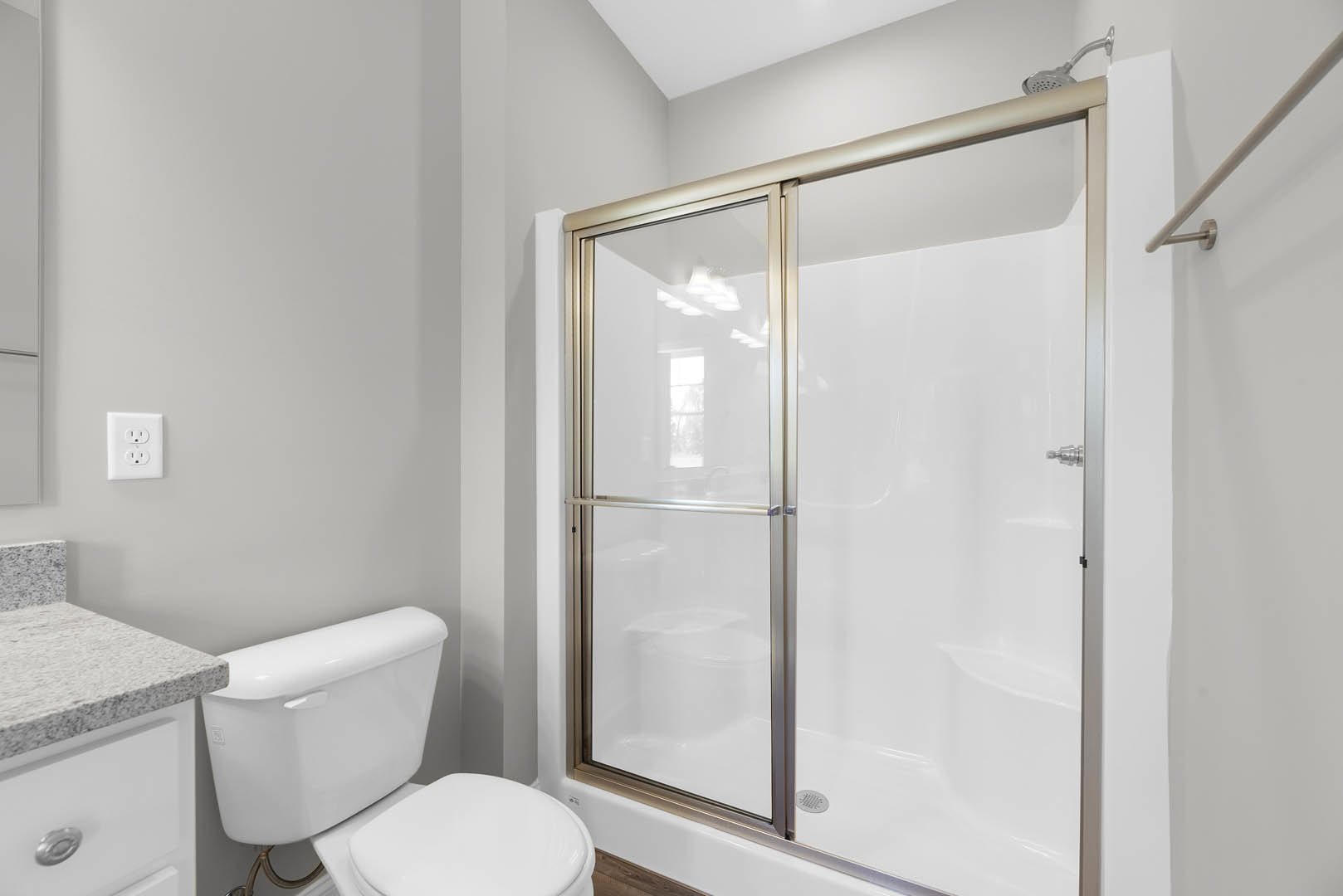 Modern bathroom featuring a glass-enclosed shower with sliding door, white toilet, light-colored tile walls, quartz countertop with built-in outlet, and sleek white drawers beneath
