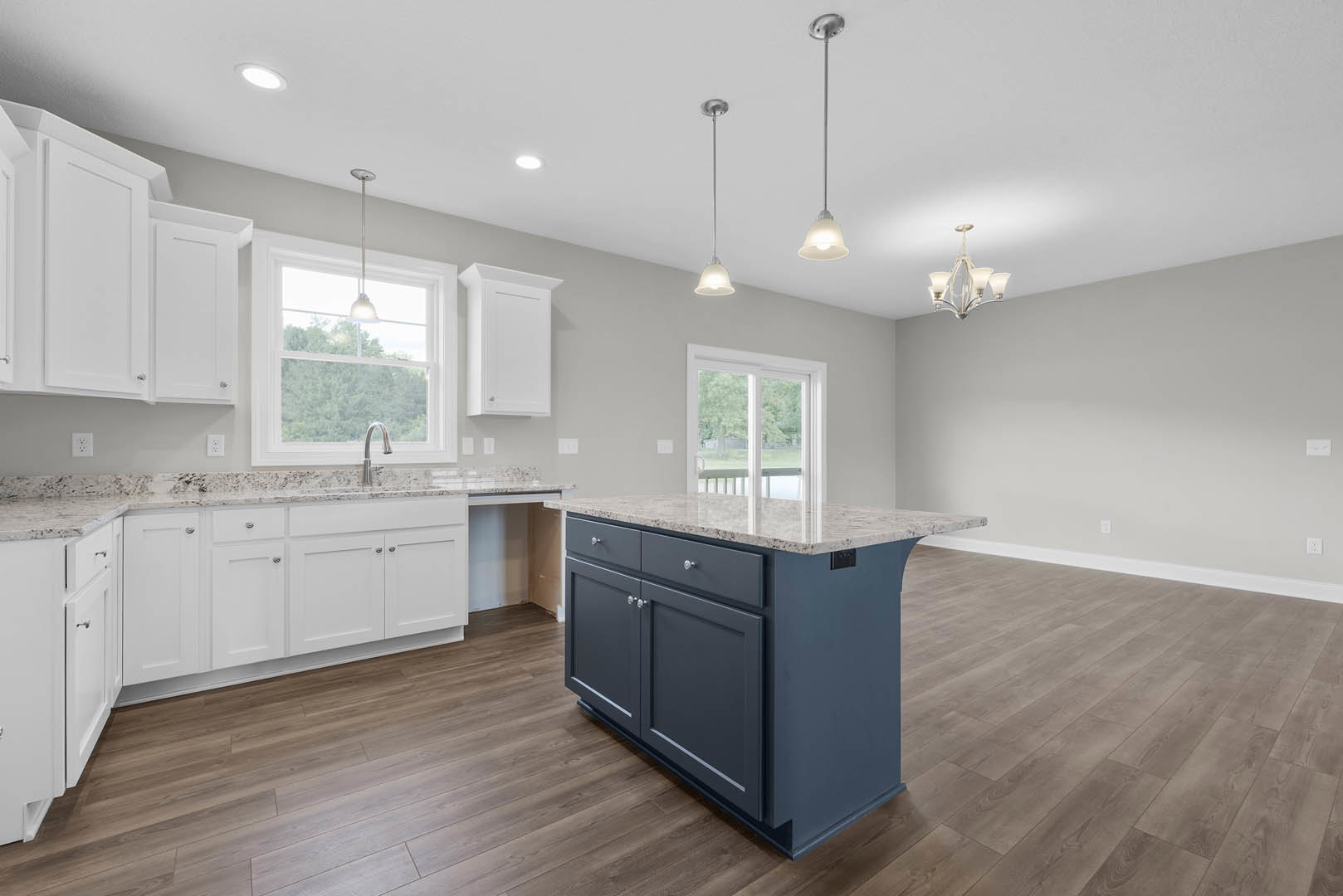 Kitchen with wood flooring, central island featuring marble countertop, white cabinetry, stainless steel appliances, pendant lighting above sink, sliding glass door in background