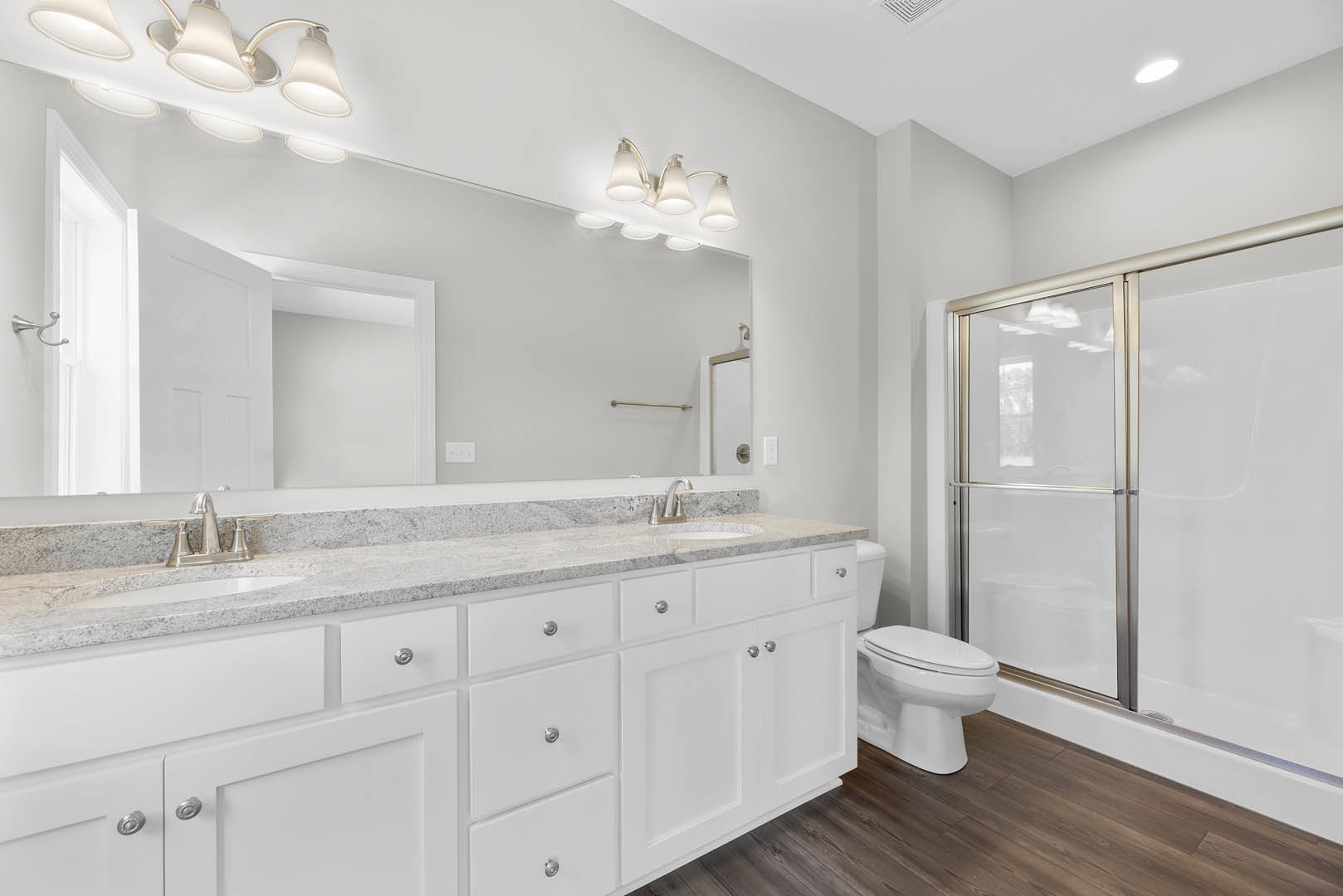 Modern bathroom featuring a rectangular mirror above a white sink with chrome faucet, light gray tile backsplash, white toilet with closed lid, glass shower door, silver wall hook