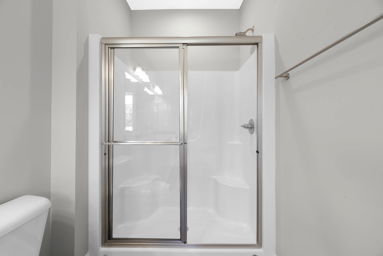 frameless glass shower enclosure with chrome hardware, white tile walls, recessed ceiling lights, and partial view of a white toilet tank