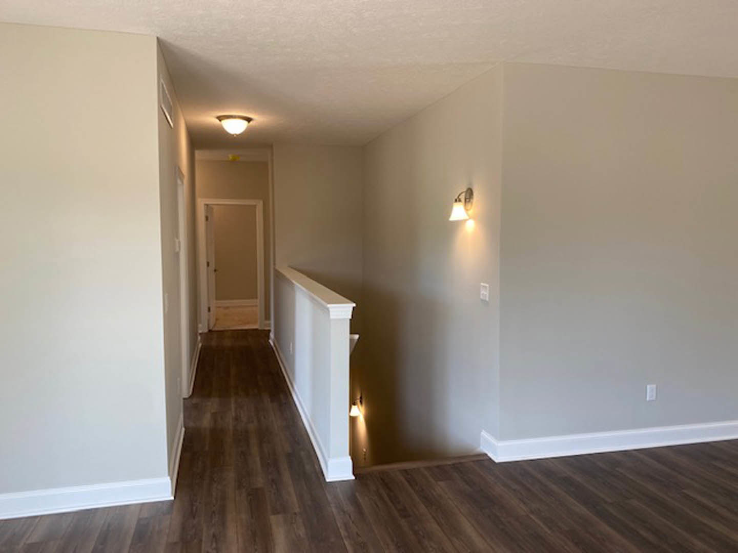 Hallway with wood flooring, white plaster walls, white door, staircase with wood steps, ceiling and wall light fixtures, decorative molding