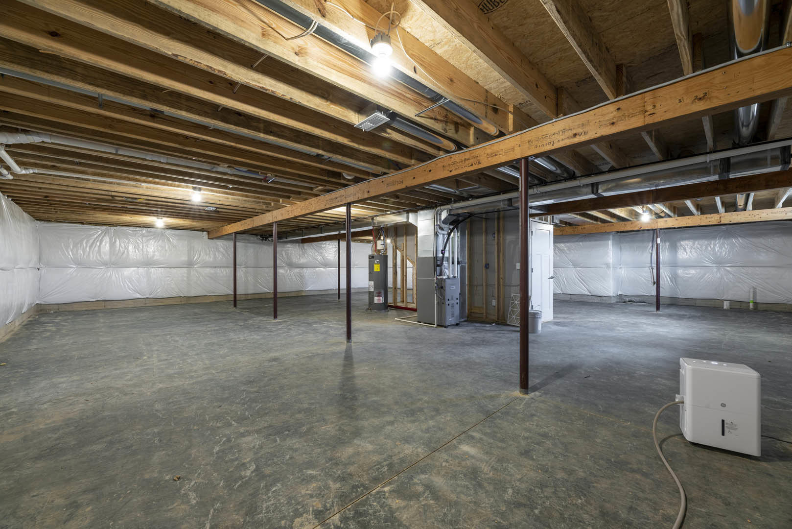 Wooden ceiling beams above a concrete floor with a central seam, metal box with black handle near white wall, ceiling light fixture visible