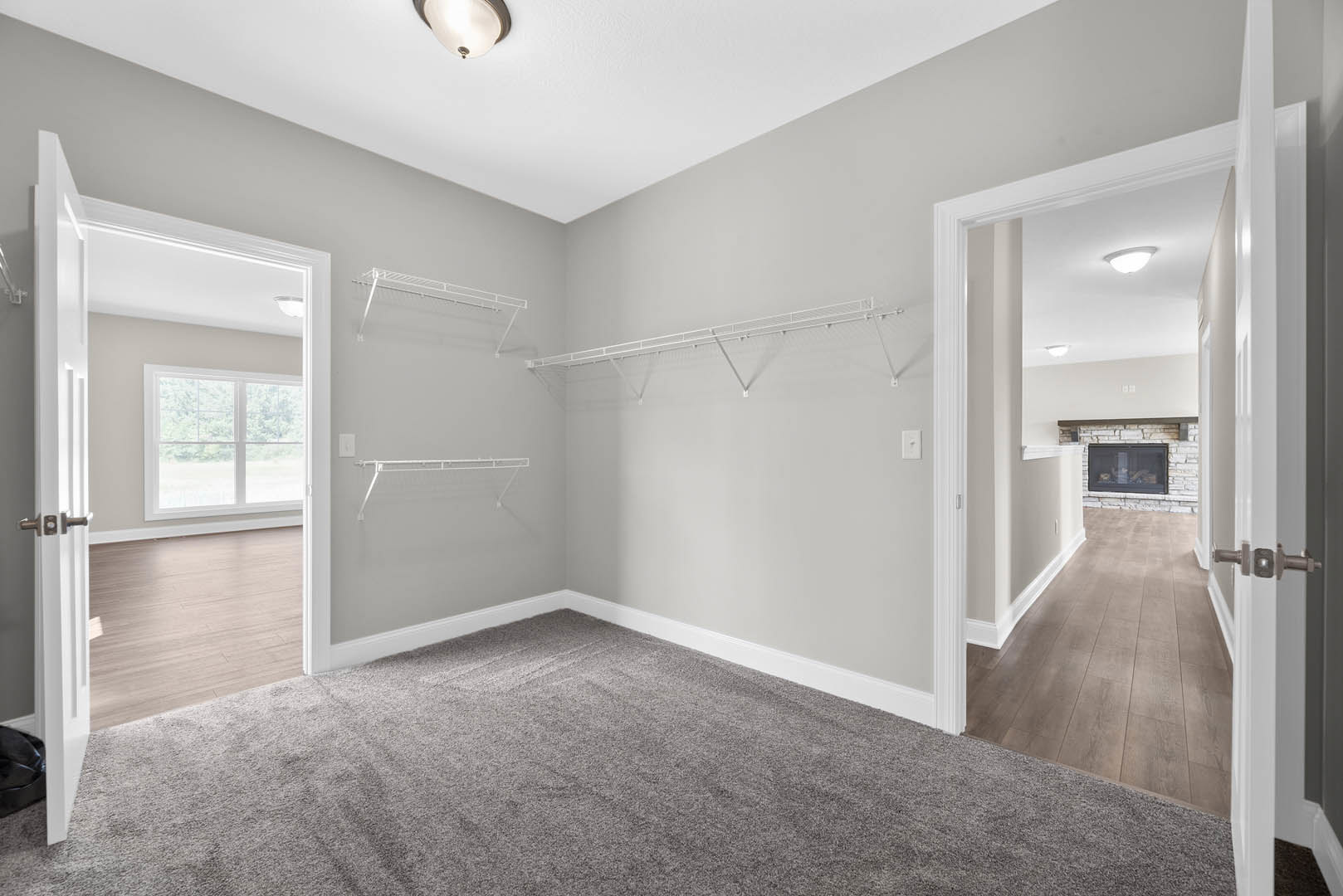 Bedroom with open white door, built-in closet, laminate flooring, white walls, window overlooking trees, ceiling molding, and white metal closet rod