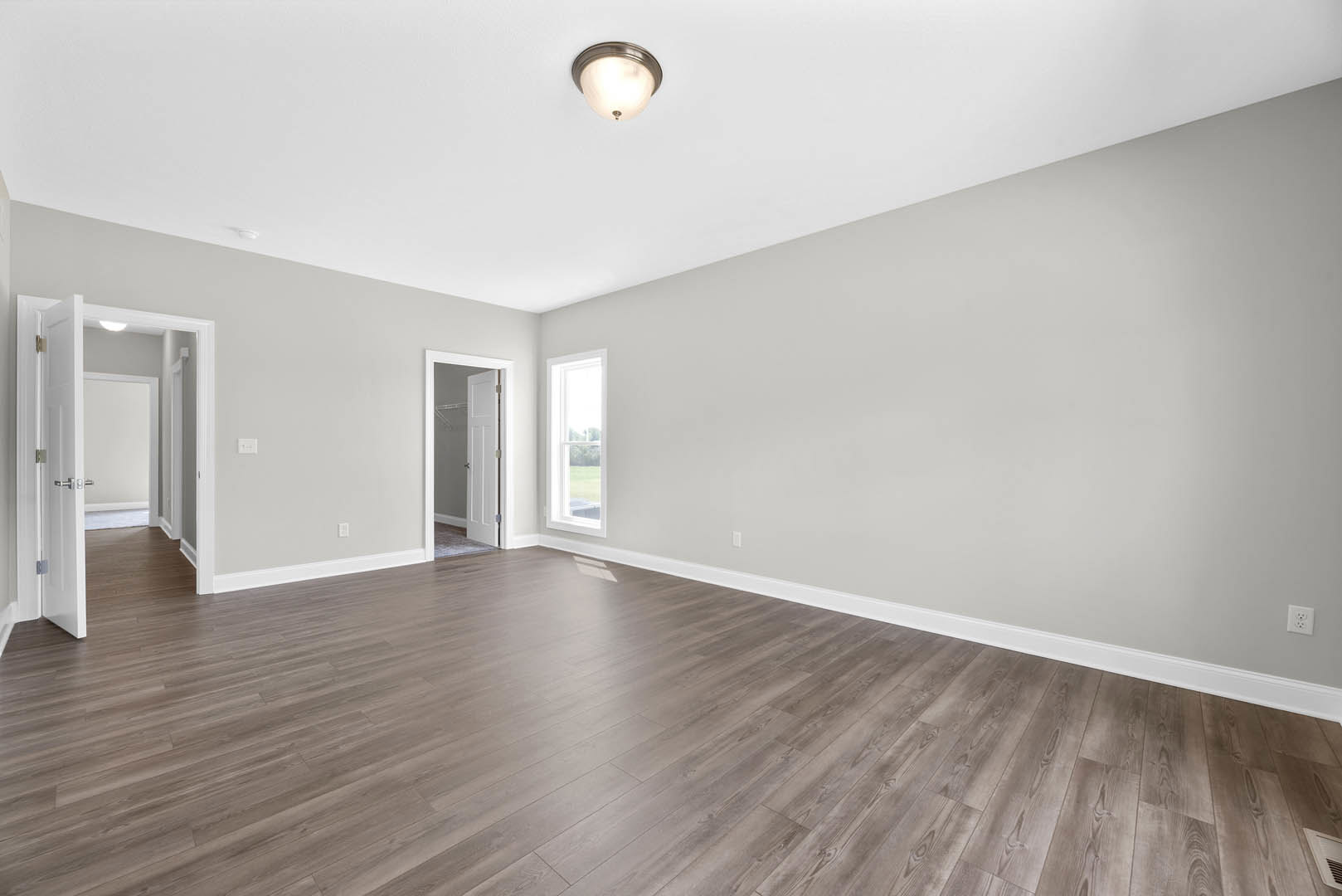 Wood flooring in a bright room with a modern ceiling light fixture, white doors, and a window overlooking a grassy field