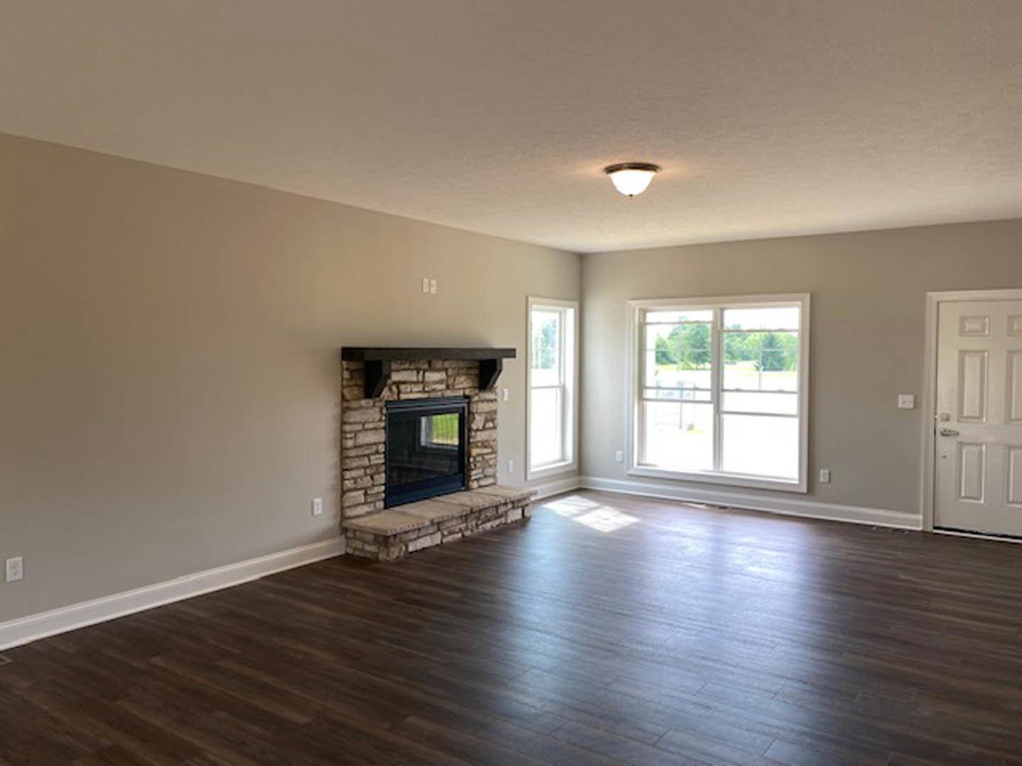 Living room with brick fireplace, wide plank hardwood floors, white door, and large window overlooking trees