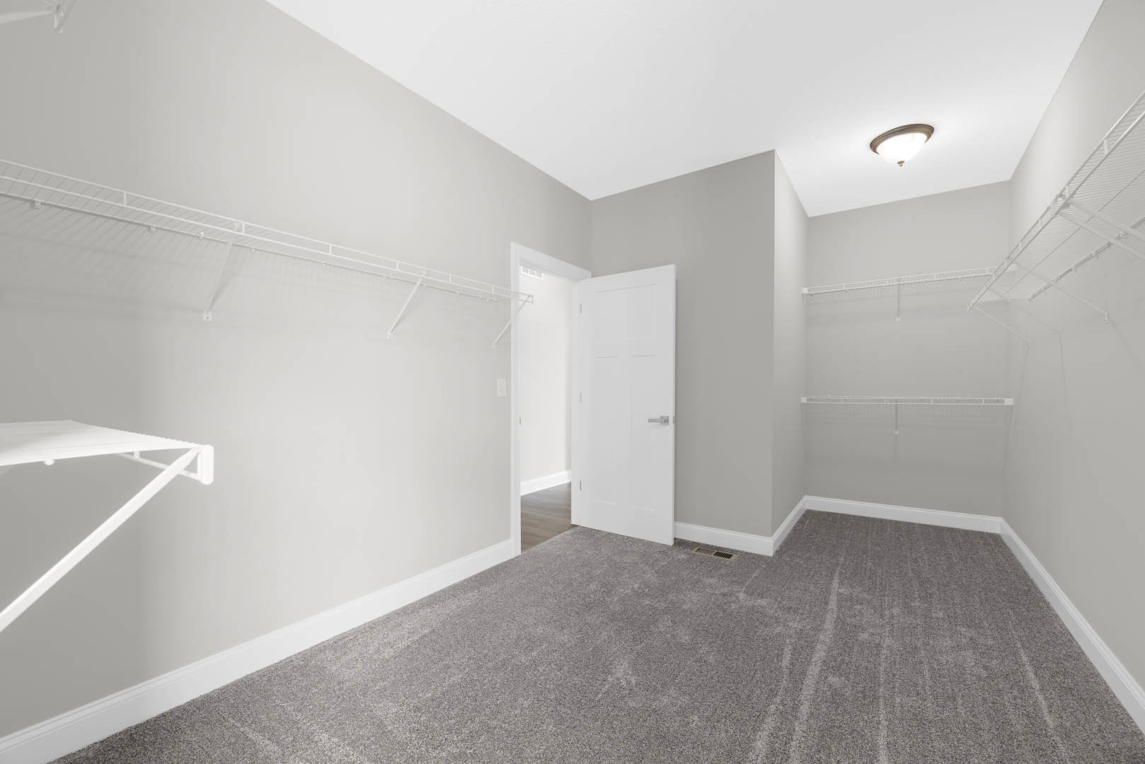 White door with silver handle, built-in white wall shelves, light fixture on white ceiling, carpeted floor, neutral walls