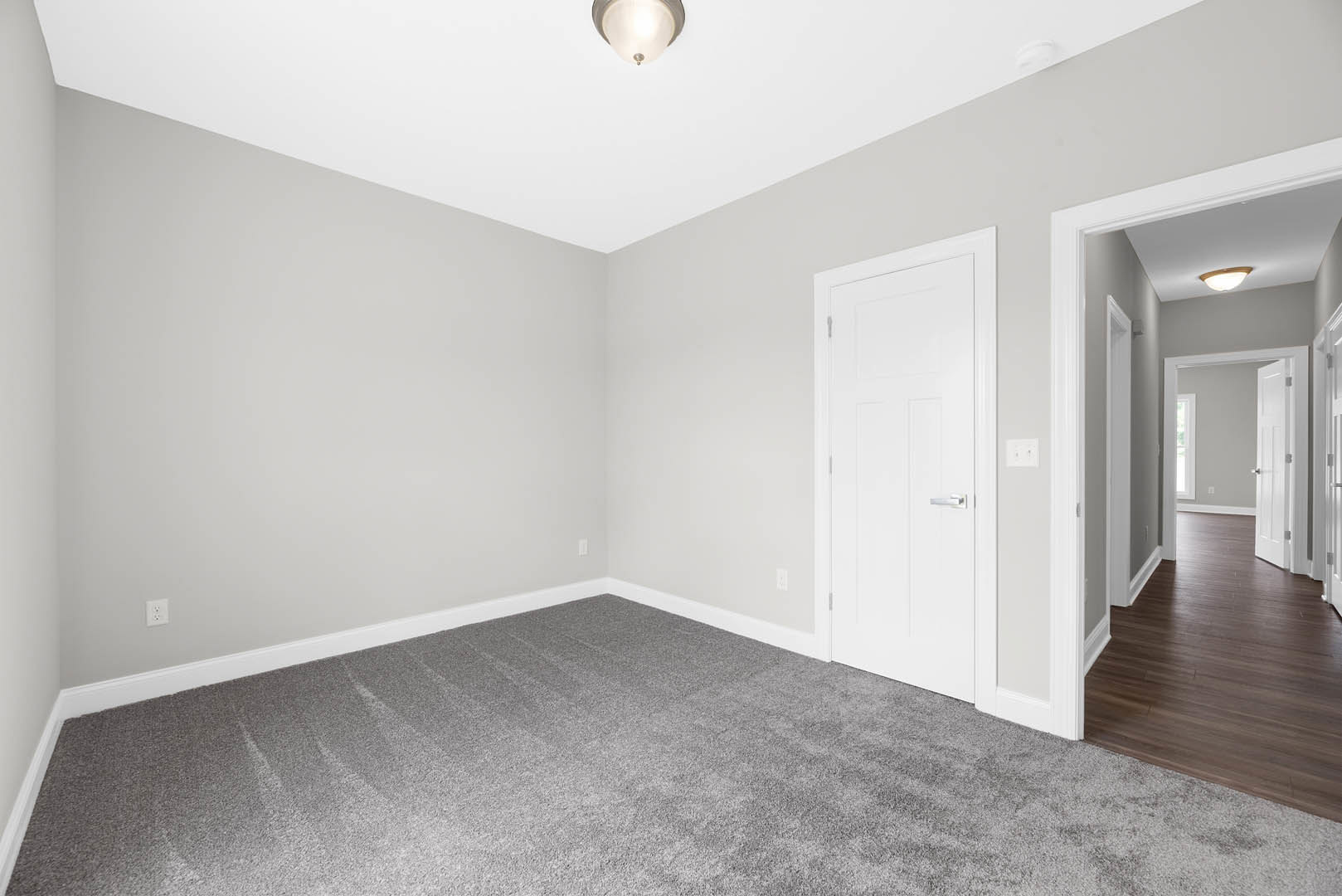 White paneled door with silver handle, grey carpet flooring, white walls, ceiling-mounted light fixture, hallway with multiple white doors