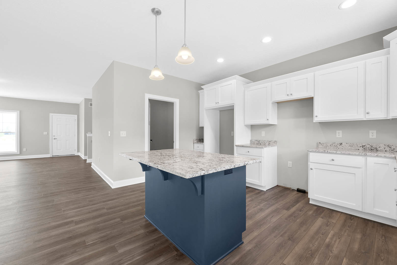 Marble kitchen island with waterfall edge, white cabinetry, stainless steel appliances, window with white trim, light wood flooring, and silver hardware