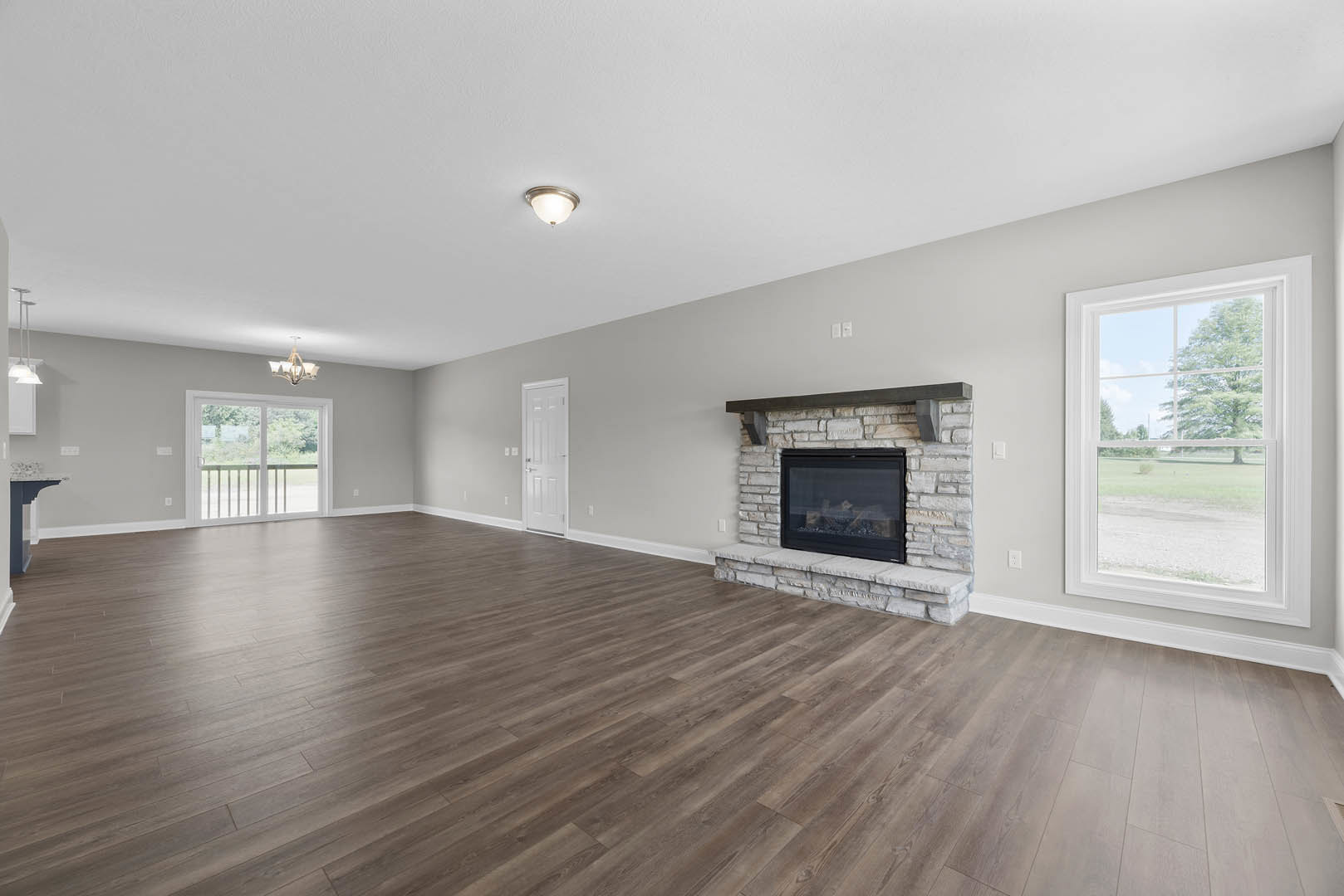 Spacious room featuring hardwood floors, central fireplace with glass door, white sliding glass door, large window overlooking field and trees, neutral walls and ceiling
