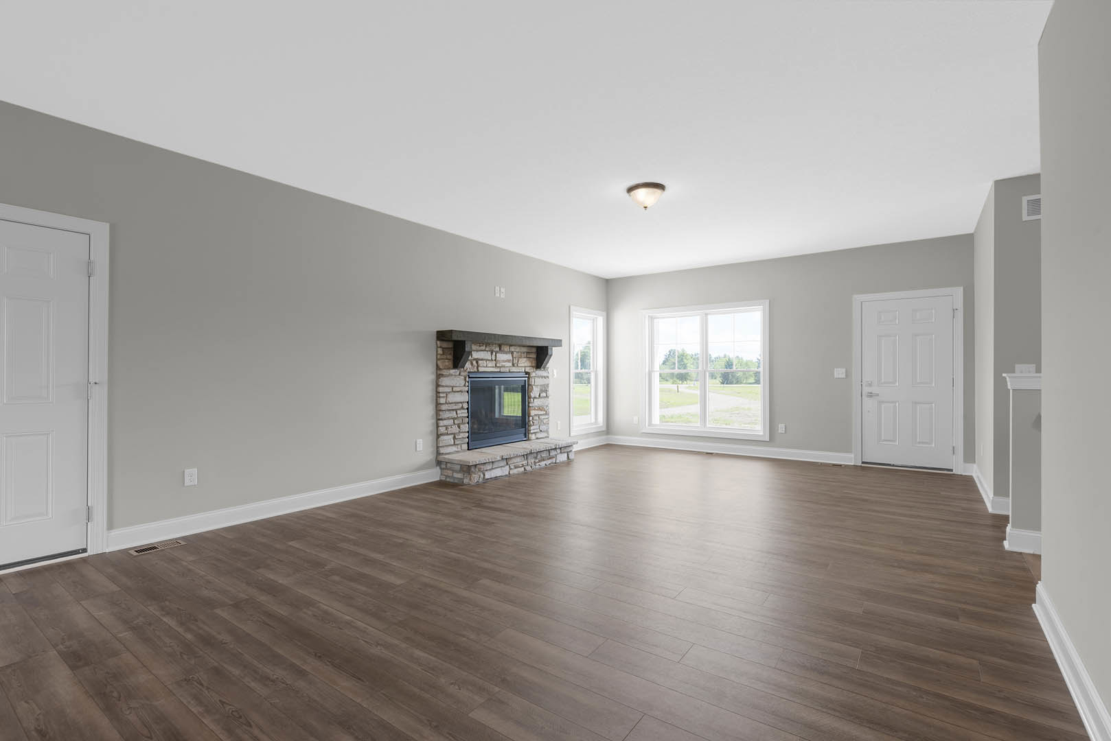 Spacious room with hardwood floors, brick accent wall featuring a window overlooking a field, central fireplace, ceiling light fixture, and white door with silver handle
