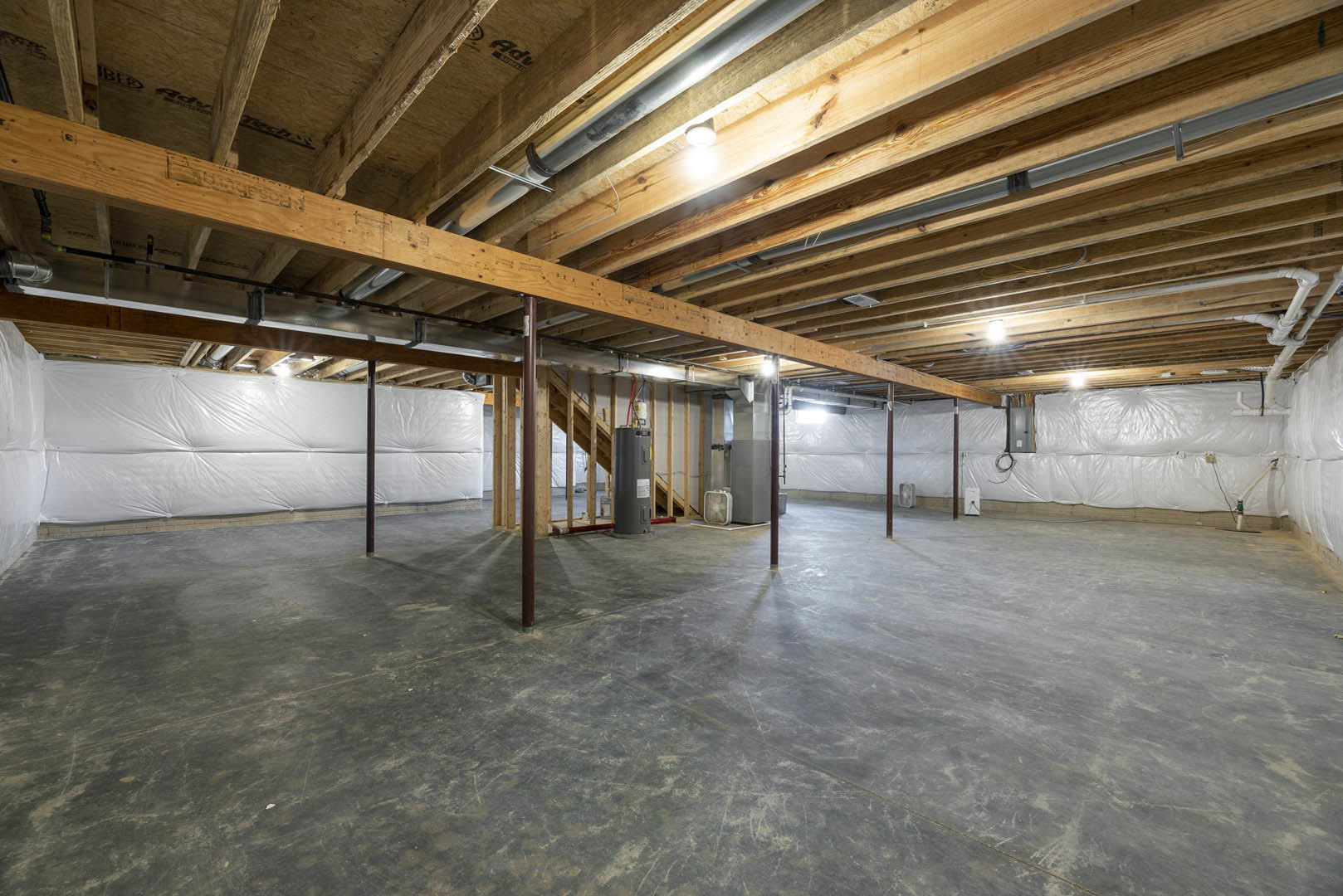 Open room with exposed wooden ceiling beams, polished concrete floor, metal support pole, wall-mounted heater, and soft overhead lighting.
