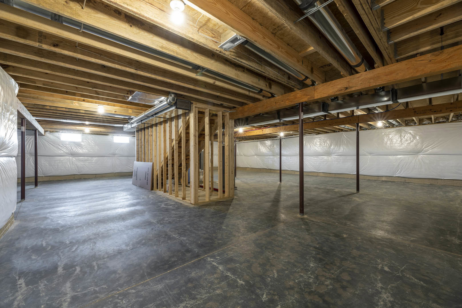 Basement with exposed wood beams and ceiling beams, concrete floor, white plastic wall covering, and ceiling light fixture