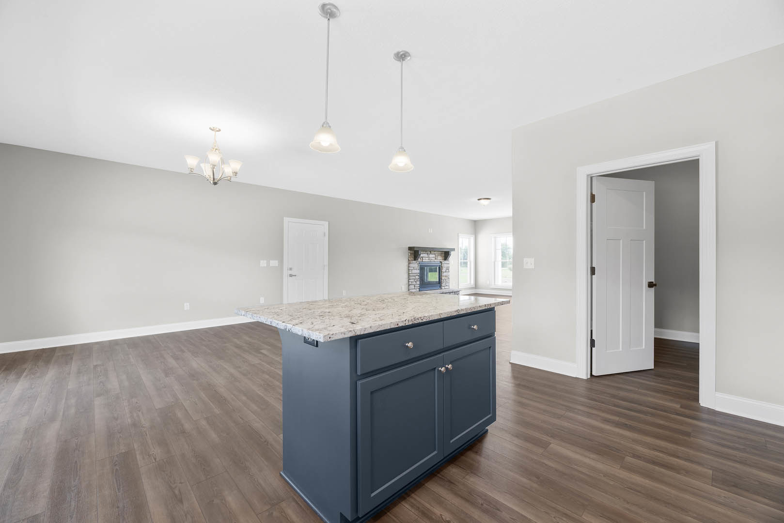 Marble-topped kitchen island with built-in sink, white cabinetry, wood flooring, and a close-up of a modern chandelier; white door with black handle visible in background.