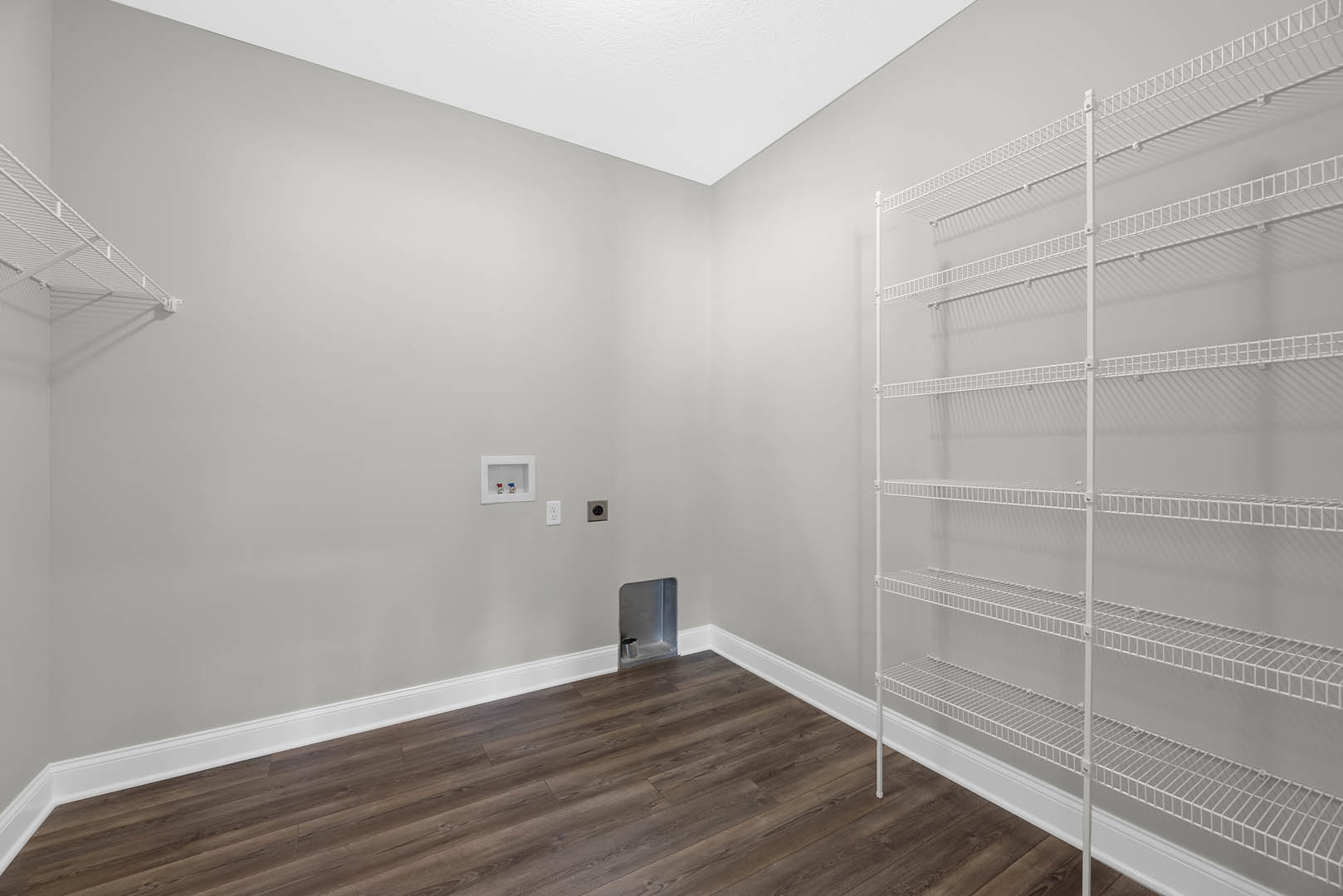 Wood flooring with white baseboards, built-in white shelves along a plaster wall, silver metal object on shelf, minimalist interior design.