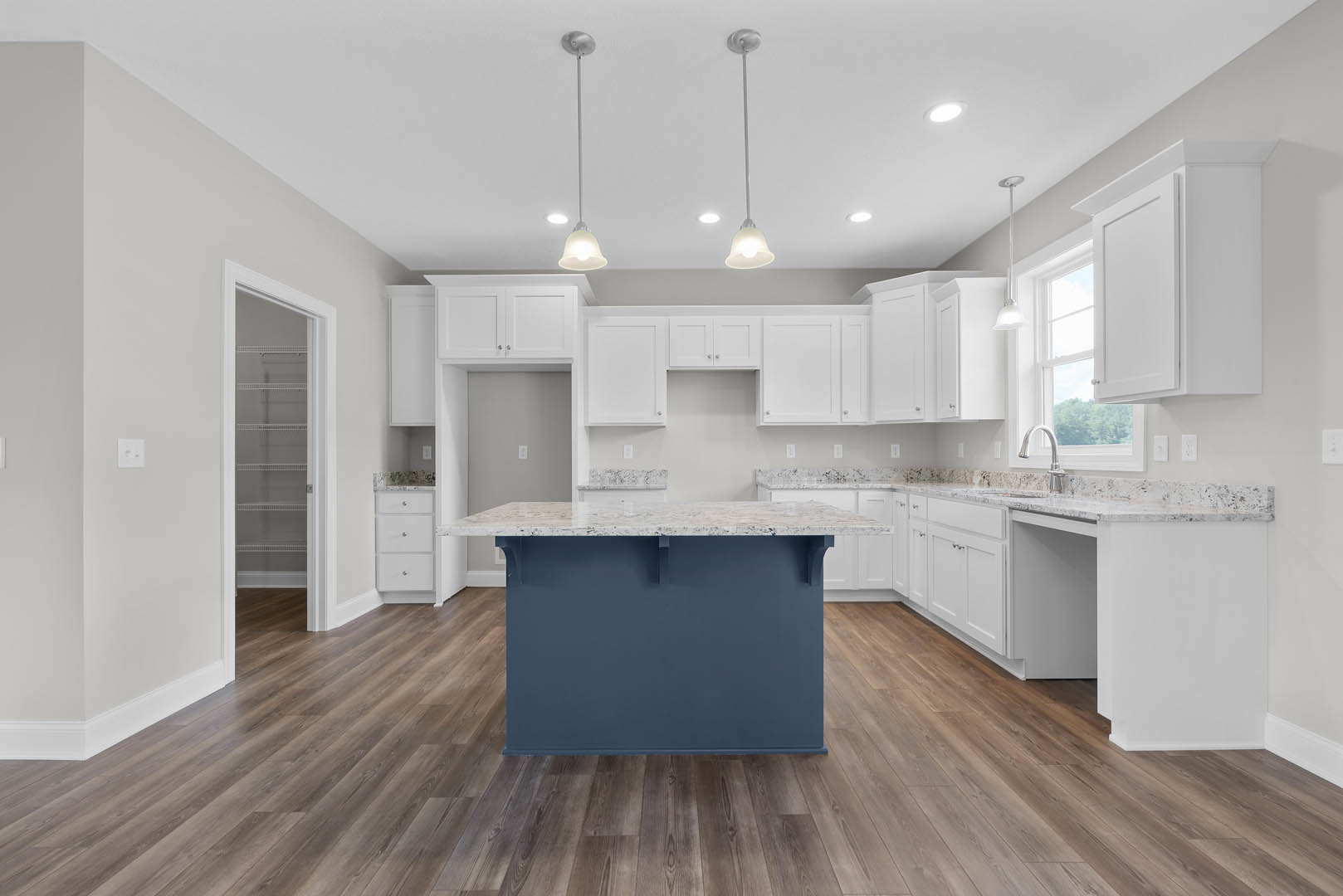 Spacious kitchen featuring a large central island with stone countertop, blue accent wall, wood flooring, white cabinetry, and stainless steel sink.
