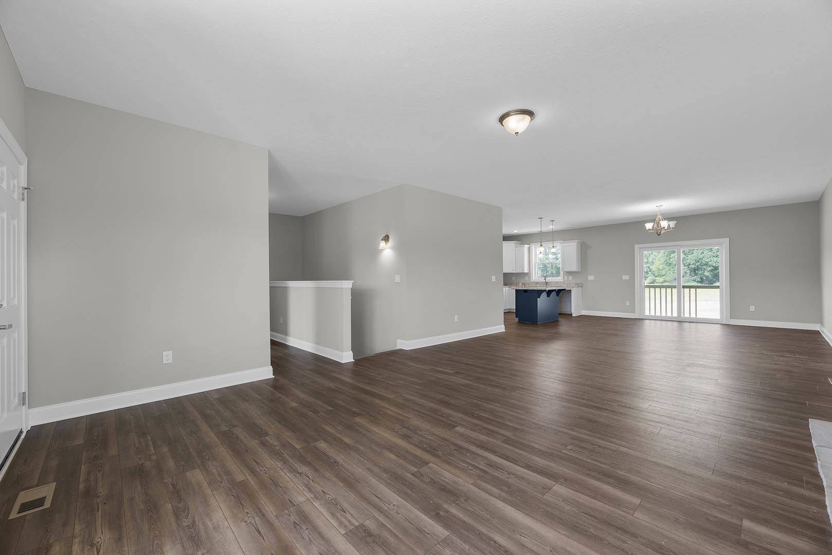 Spacious room with wood flooring, white walls and trim, ceiling light fixture, window with railing, and wall vent