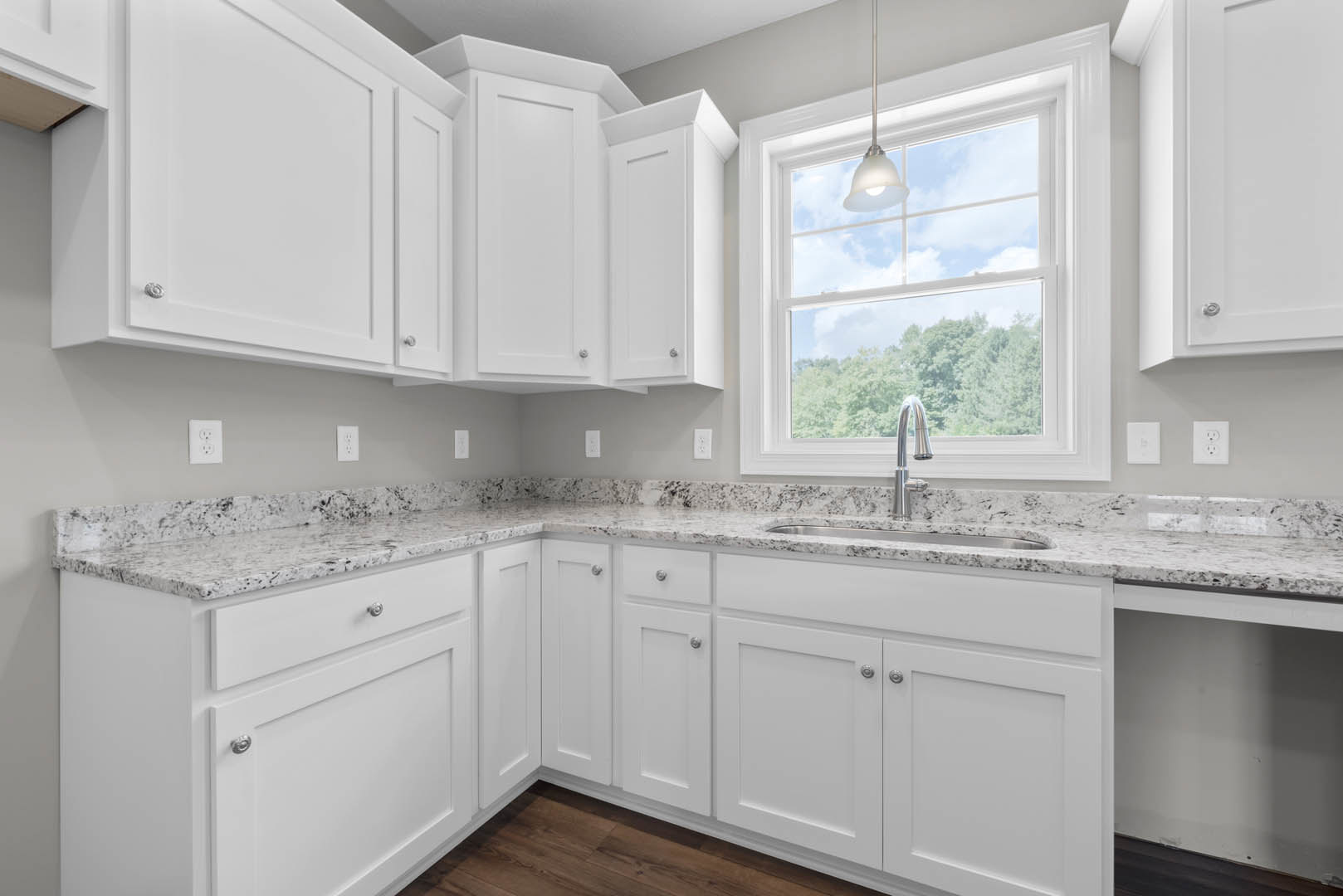 White kitchen cabinets with granite countertops, stainless steel sink beneath ceiling light, white electrical outlets on wall, close-up of chrome faucet, drawers and cupboards