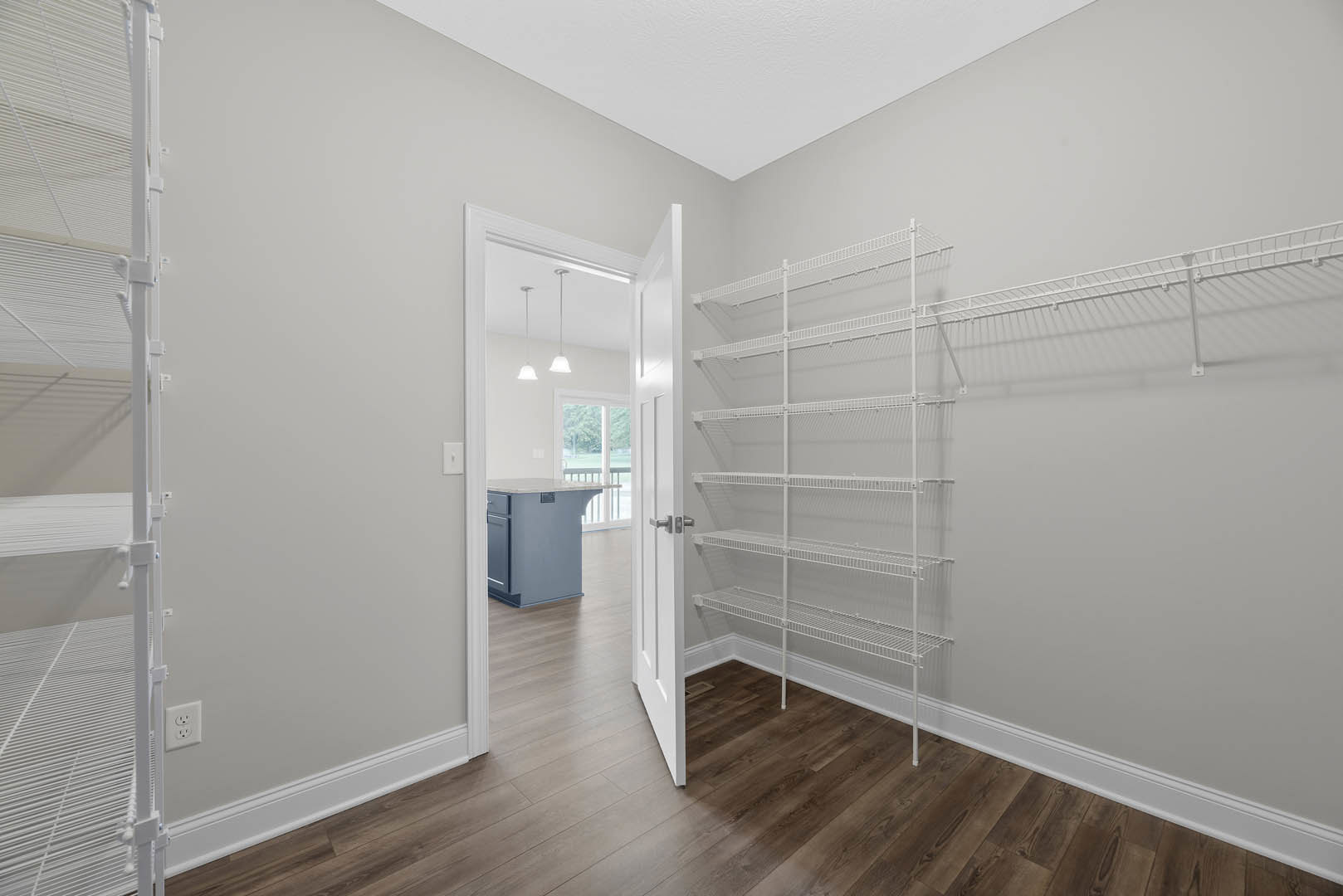 Open white door leading to a room with white shelves built into a plaster wall, light wood flooring, and minimalist cabinetry.