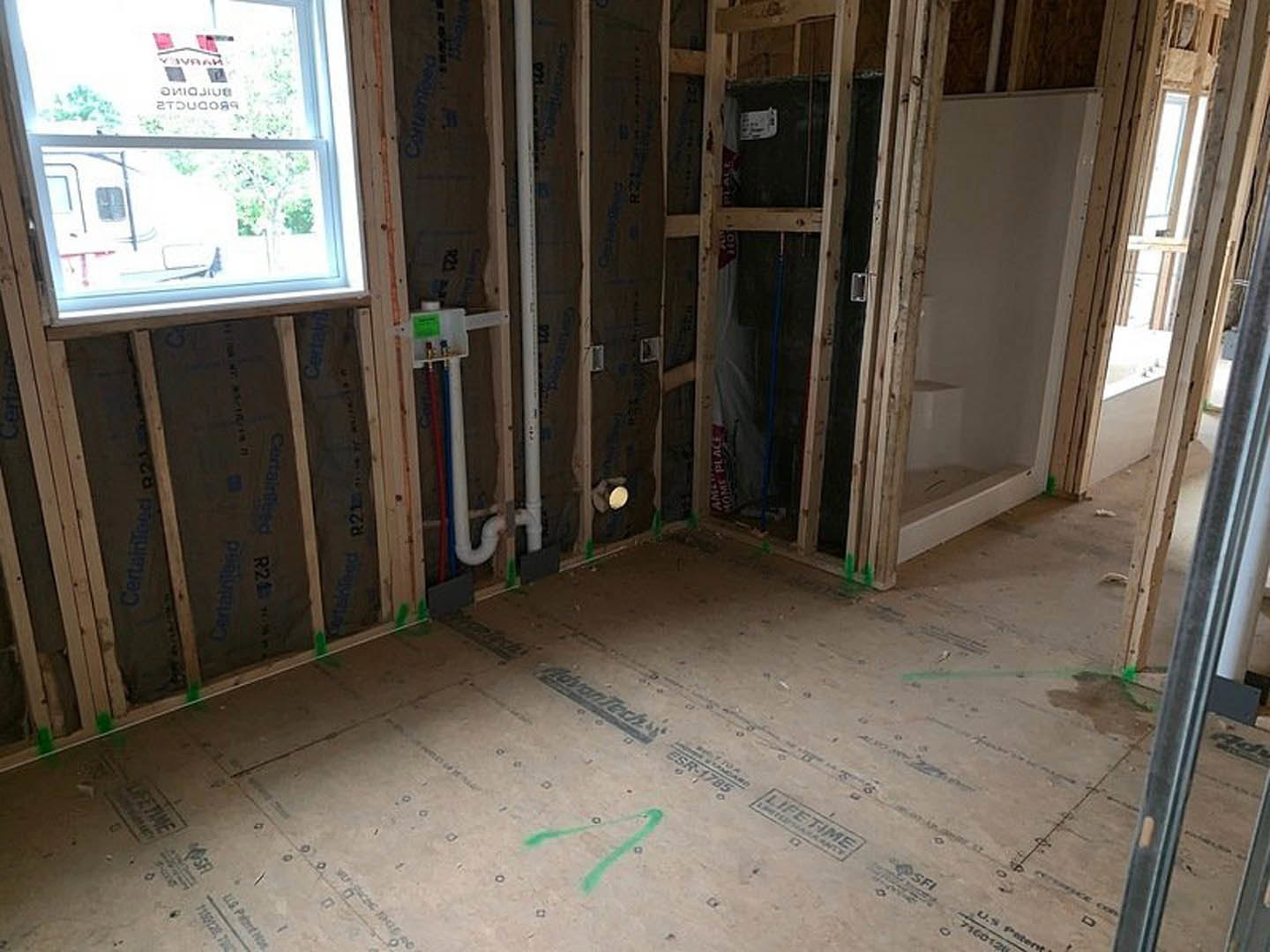 Room under construction featuring unfinished wood walls, a window with a sign, white surfaces marked with green paint, and a recessed shelf.
