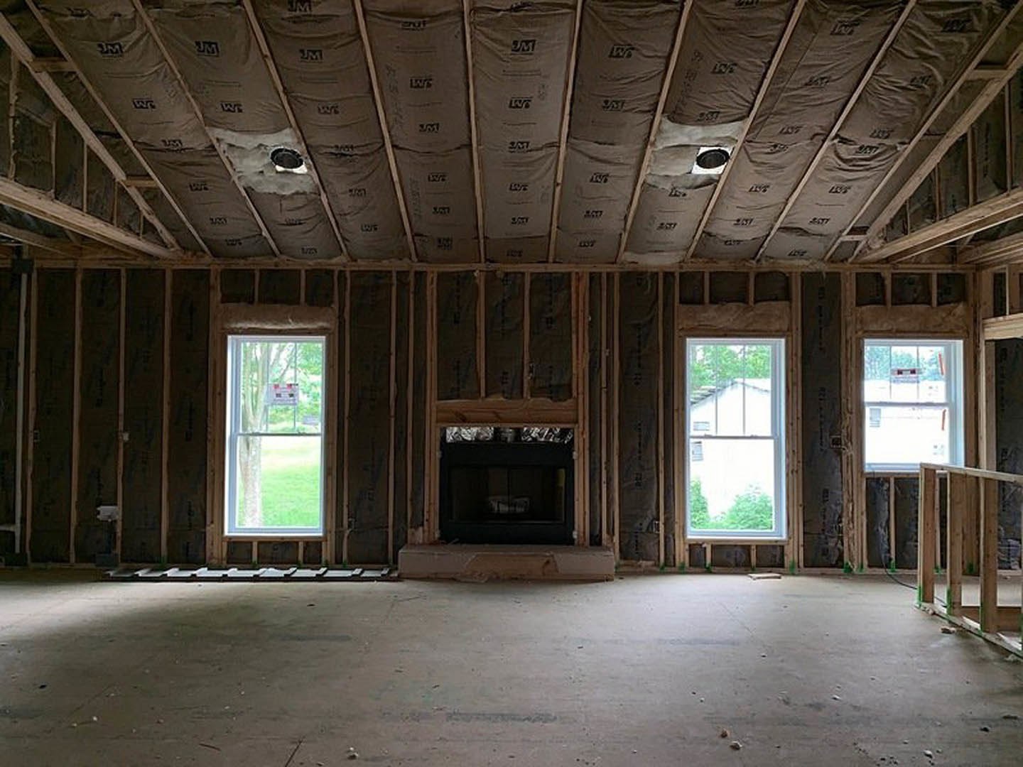 Living room with concrete floor, exposed wooden ceiling beams, white-framed windows, and a central fireplace