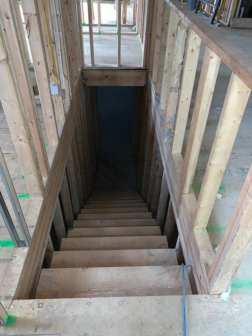 Wooden staircase with metal handrail, wood plank steps, and exposed wood framing in a room with unfinished concrete floor