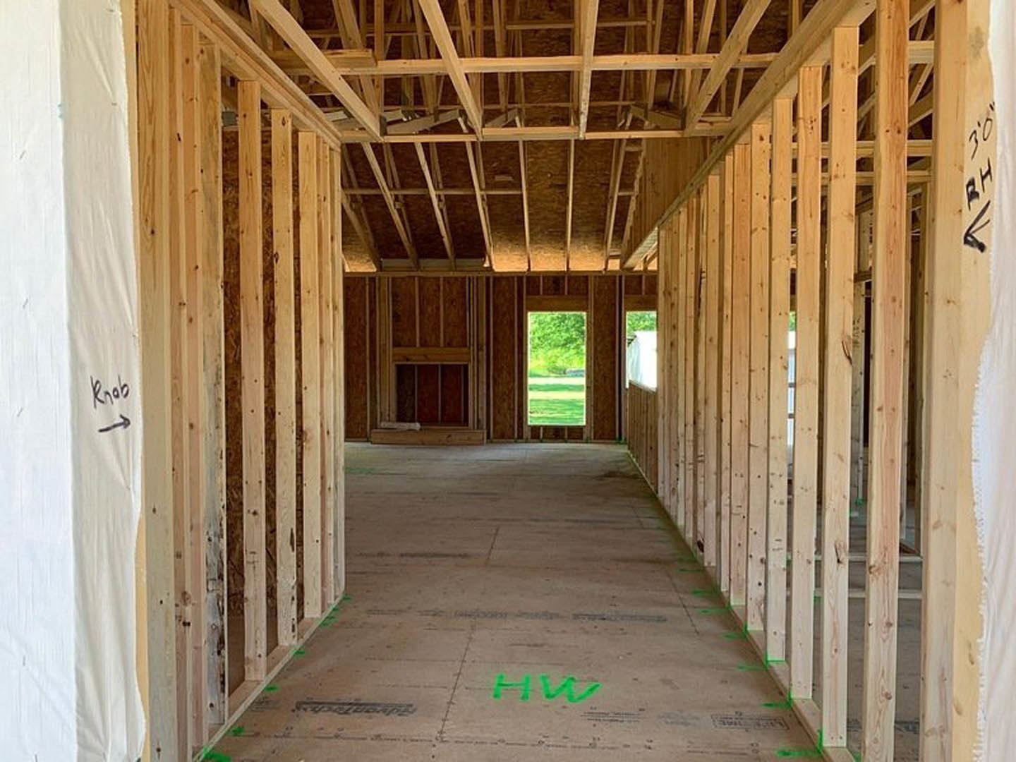 Hallway with exposed wood framing, concrete floor painted green, window overlooking grassy field, green letter sign on surface