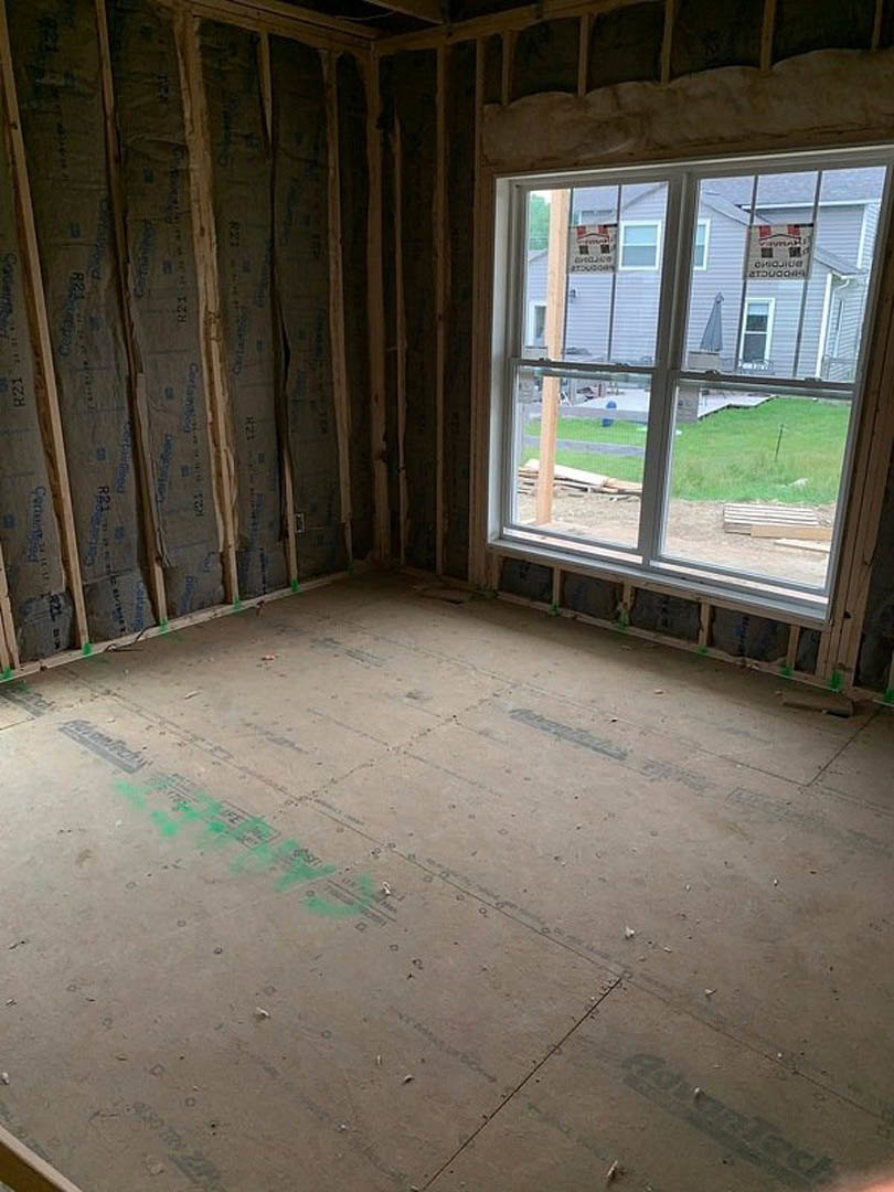Room with two windows, green painted floor, wood trim, and a sign posted on one window with yard visible outside