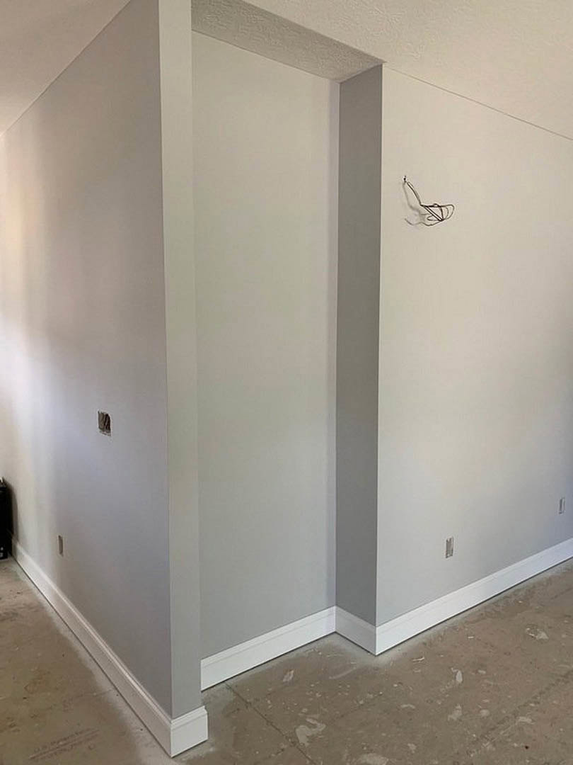 White plaster wall with recessed doorway, light fixture, and visible corner detail in a modern room with hardwood flooring and smooth ceiling.