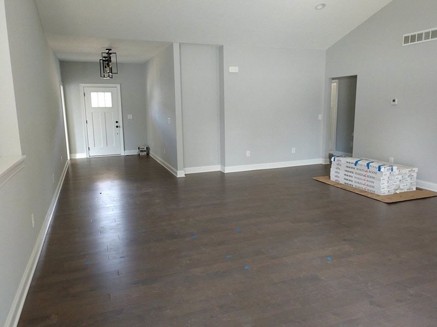 Wood flooring with blue paint accents, white door featuring a window, white vent on wall, stack of white books, plaster walls, and ceiling.