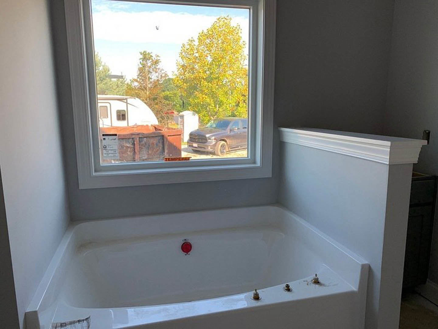 Freestanding white bathtub with chrome faucet beside large window overlooking trees, light-colored walls, and tiled floor in modern bathroom