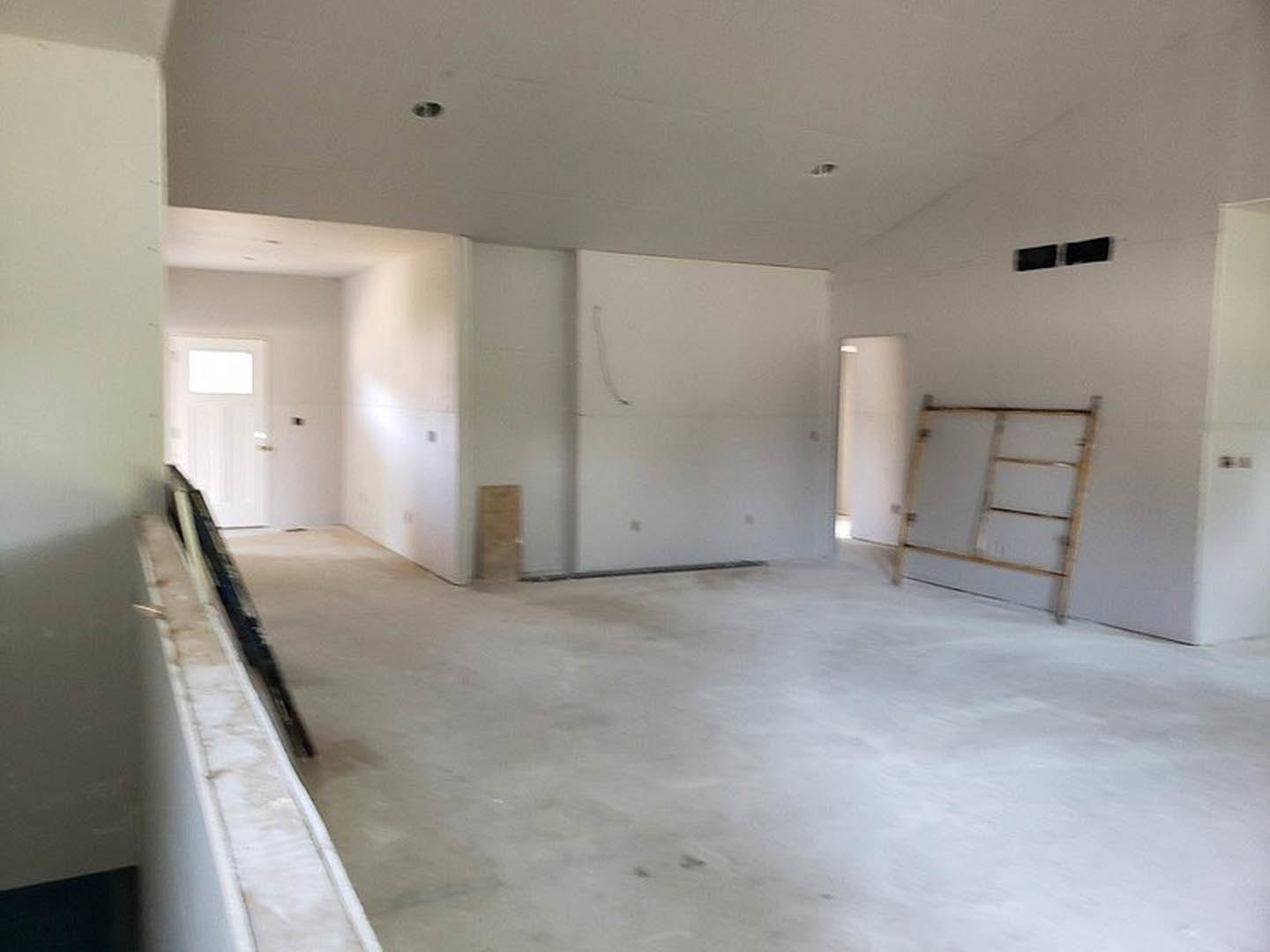 Open room with white plaster walls, light wood flooring, exposed wooden framing, and two ladders positioned near the wall.